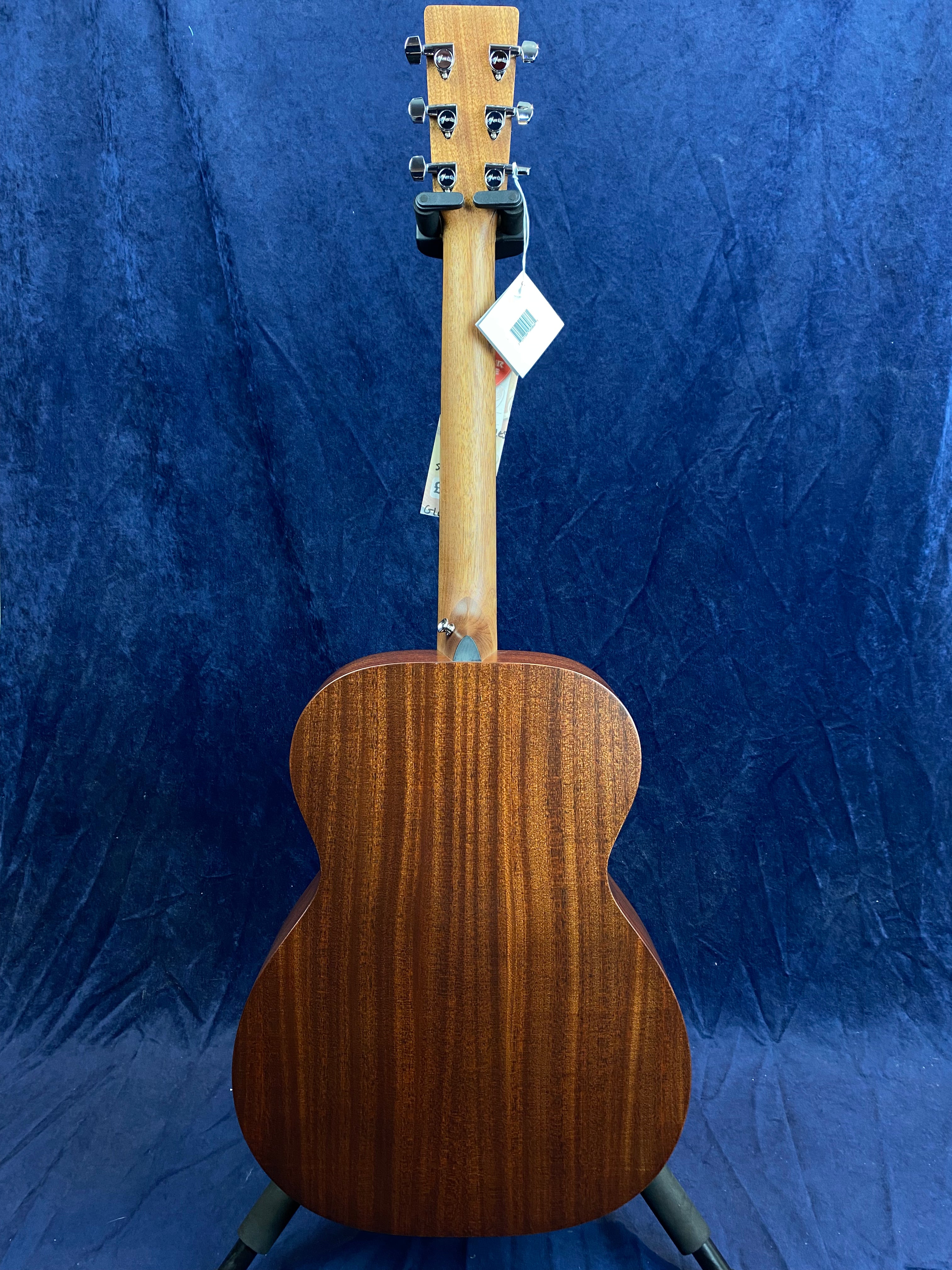 Acoustic guitar shown from the back, displaying a smooth, dark wood grain body and neck with metal tuning pegs and a price tag hanging from the headstock.