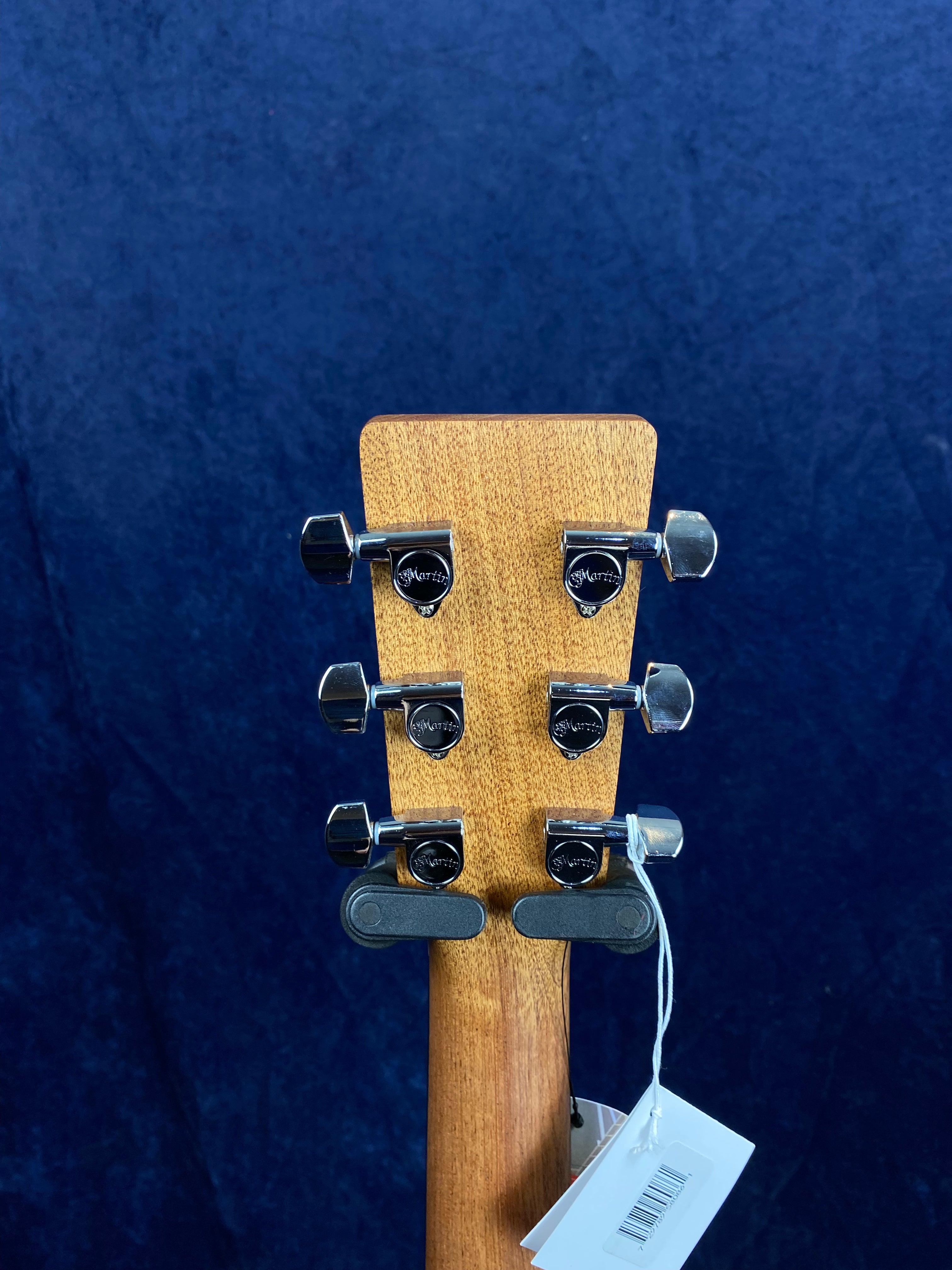 Six chrome tuning pegs on the headstock of an acoustic guitar, with a wooden finish and two tags attached by a white string.