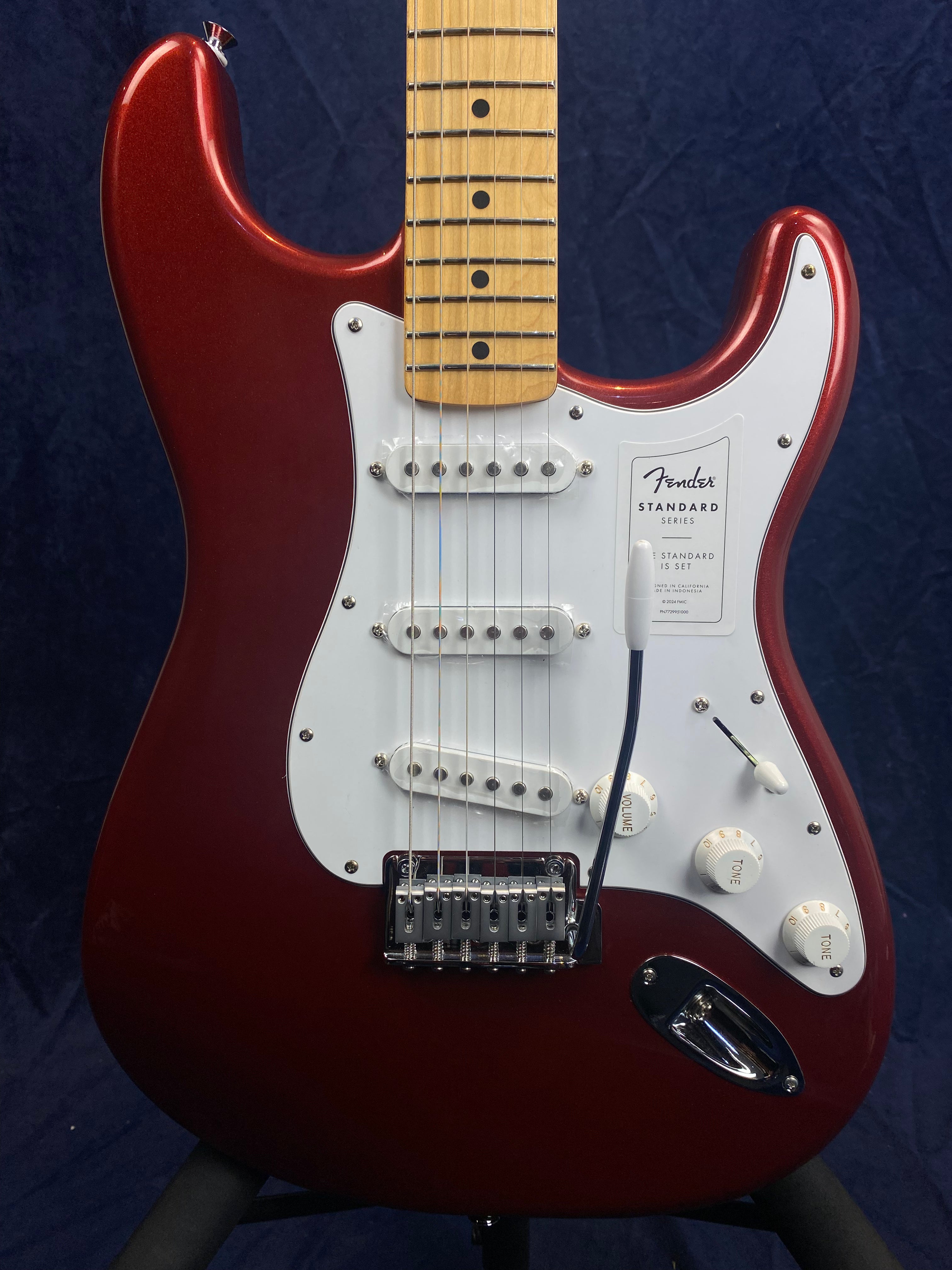 Red Fender electric guitar with a white pickguard, three single-coil pickups, five-way switch, three white control knobs, and a maple fretboard.