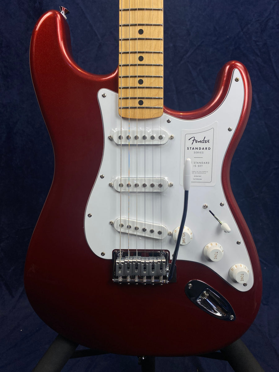 Red Fender electric guitar with a white pickguard, three single-coil pickups, five-way switch, three white control knobs, and a maple fretboard.