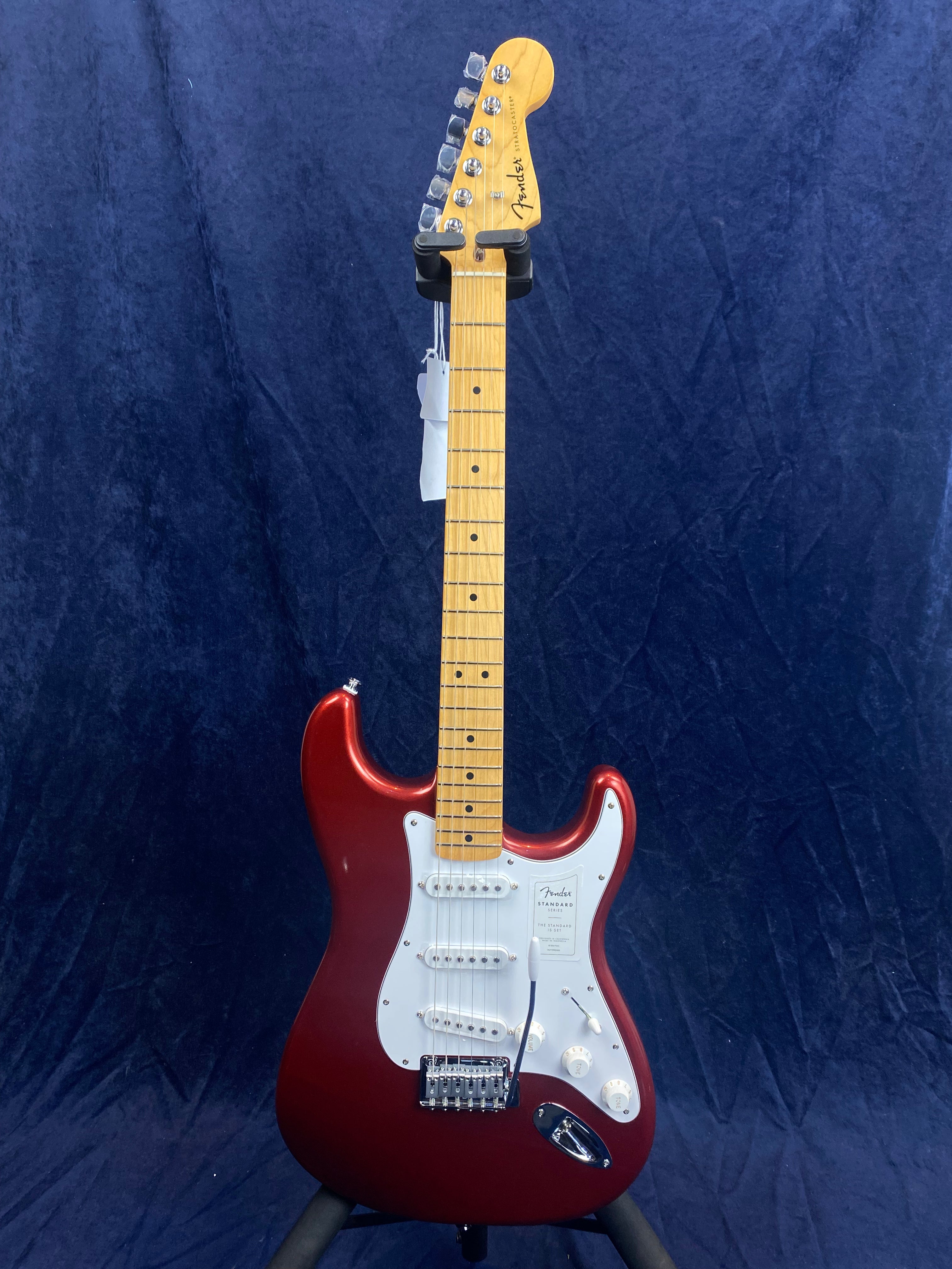 Red electric guitar with a white pickguard, three single-coil pickups, maple neck, and six tuning pegs on a light wood headstock.