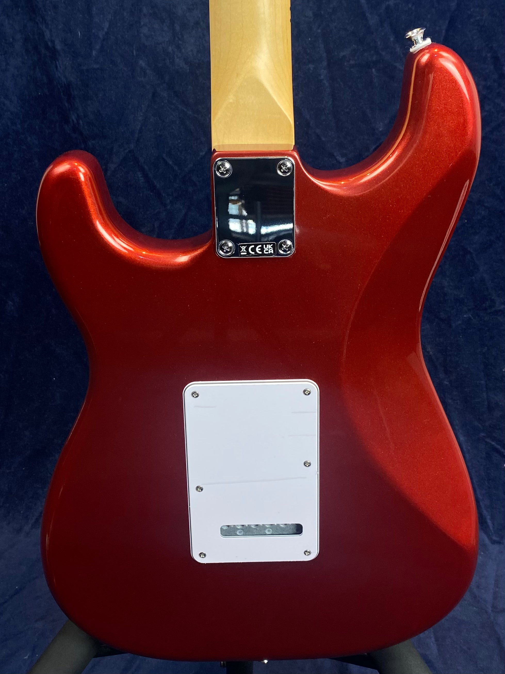 Back of a red electric guitar with a light maple neck, a white rectangular cover plate, and a metal neck plate with screws.