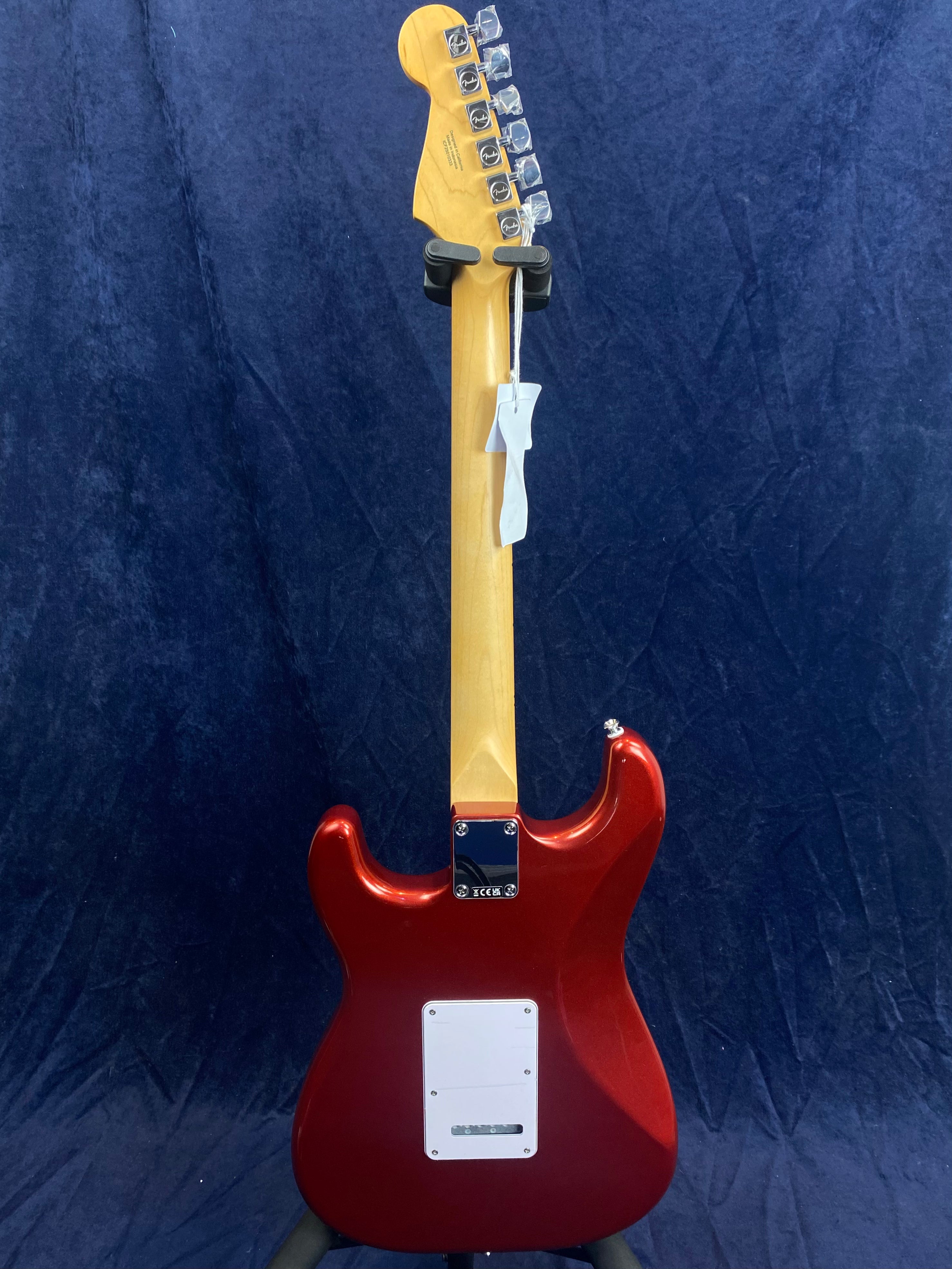 Red electric guitar viewed from the back, showing a light wood neck, six tuning pegs, and a white rectangular backplate near the bottom.