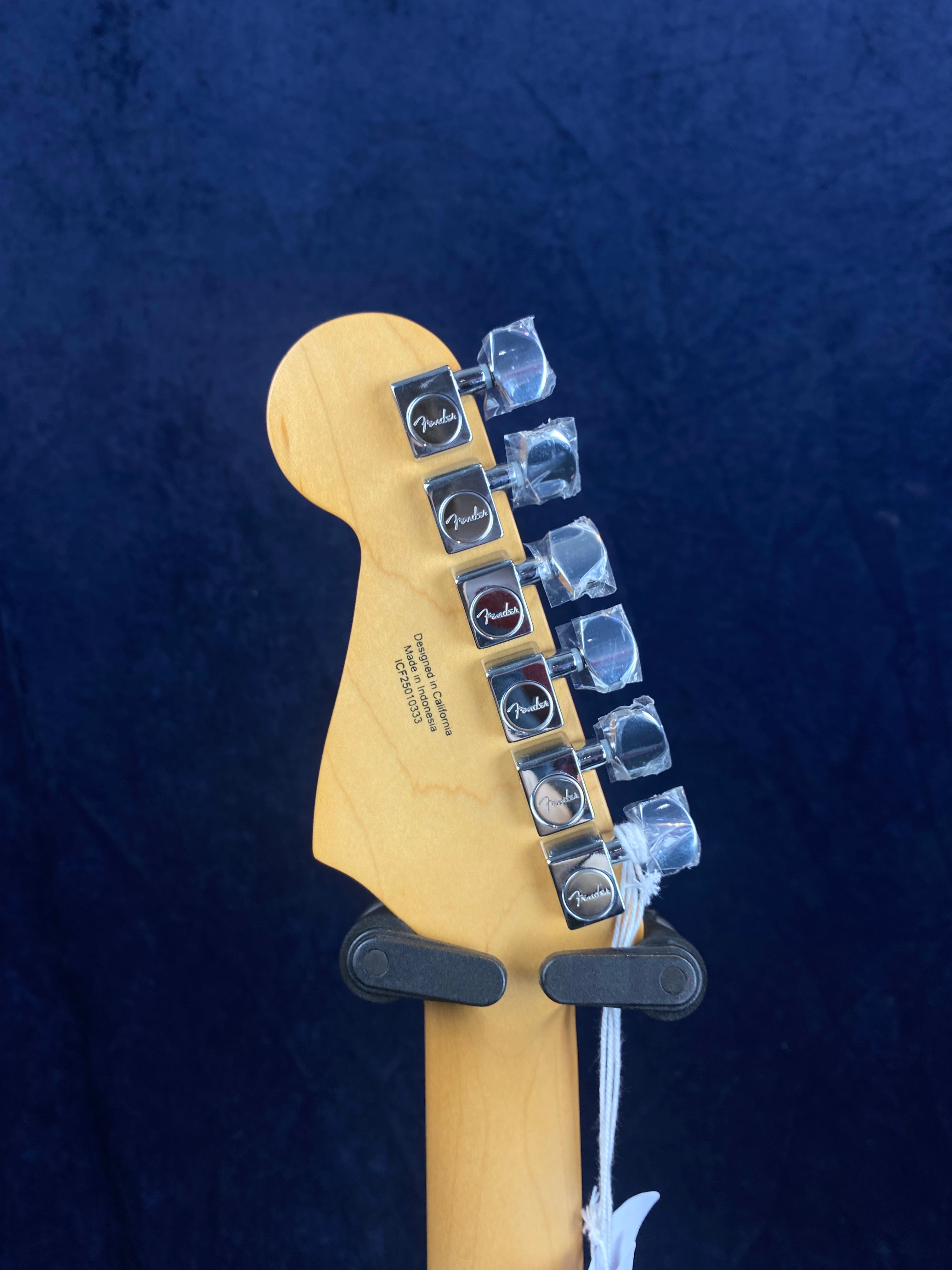 The back of a Fender electric guitar headstock with six chrome tuning pegs, some covered in protective plastic.