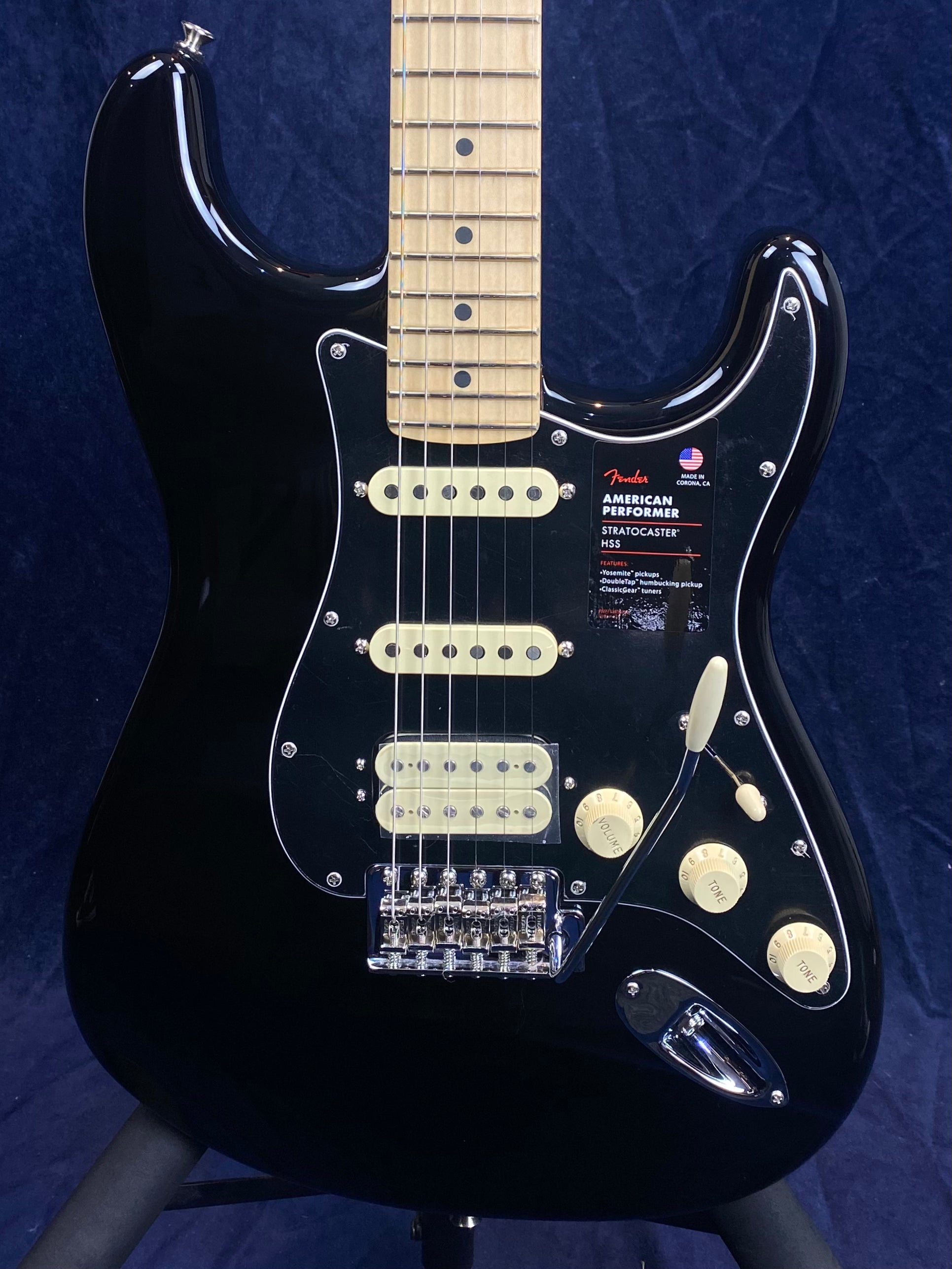 Black Fender Stratocaster electric guitar with a maple neck, three pickups, cream controls, and a tremolo arm against a dark background.