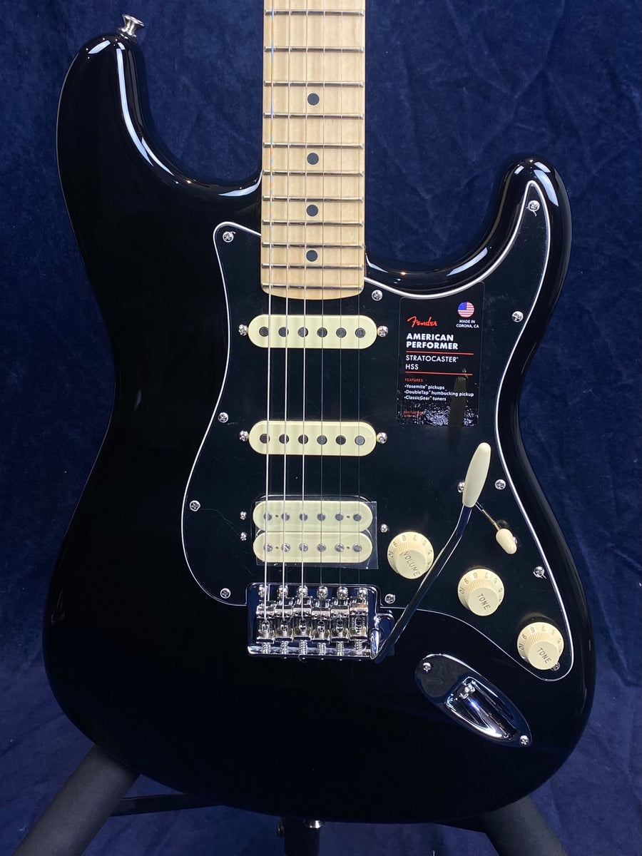 Black Fender Stratocaster electric guitar with a maple neck, three pickups, cream controls, and a tremolo arm against a dark background.