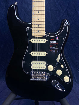 Black Fender Stratocaster electric guitar with a maple neck, three pickups, cream controls, and a tremolo arm against a dark background.