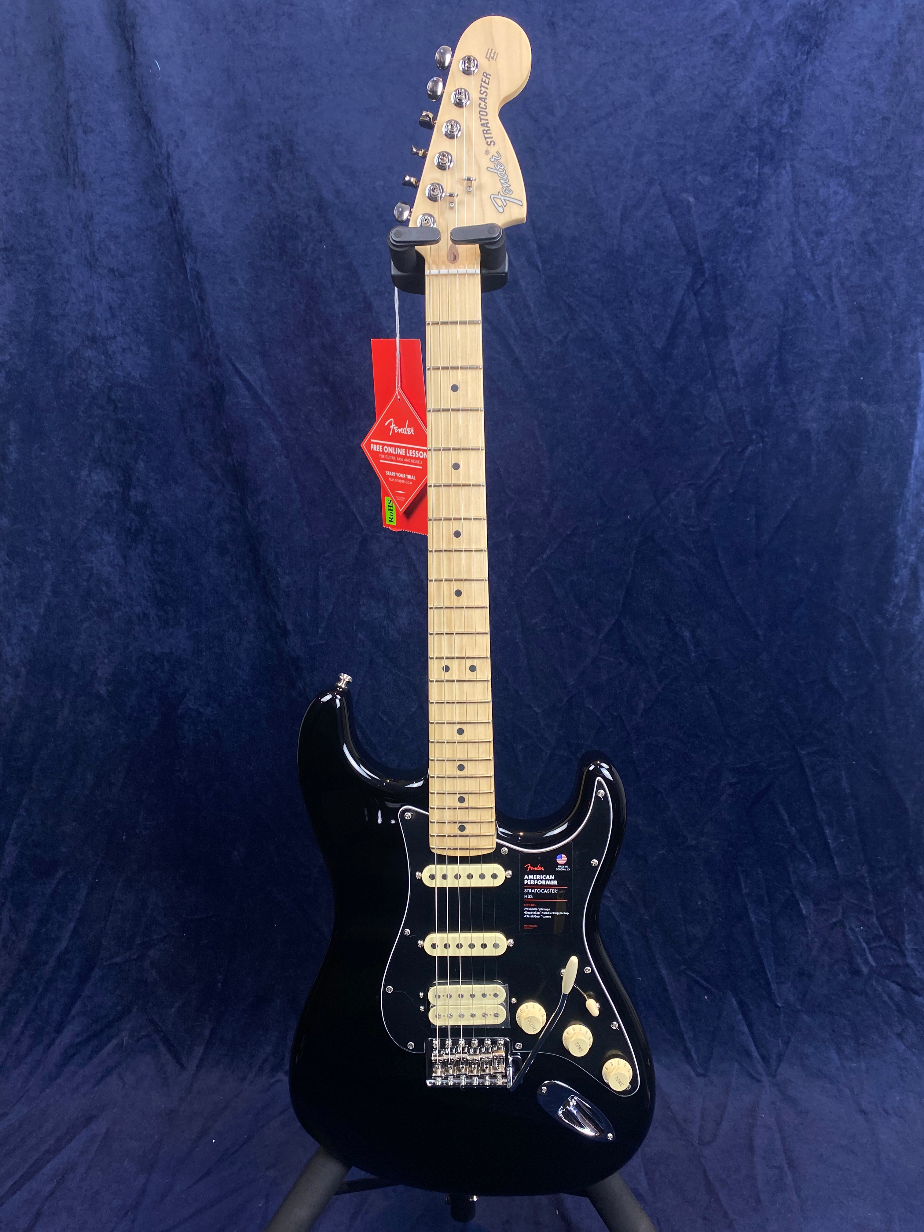 Black Fender Stratocaster electric guitar with a maple neck and fretboard, white pickups and knobs, and red tags hanging from the headstock.