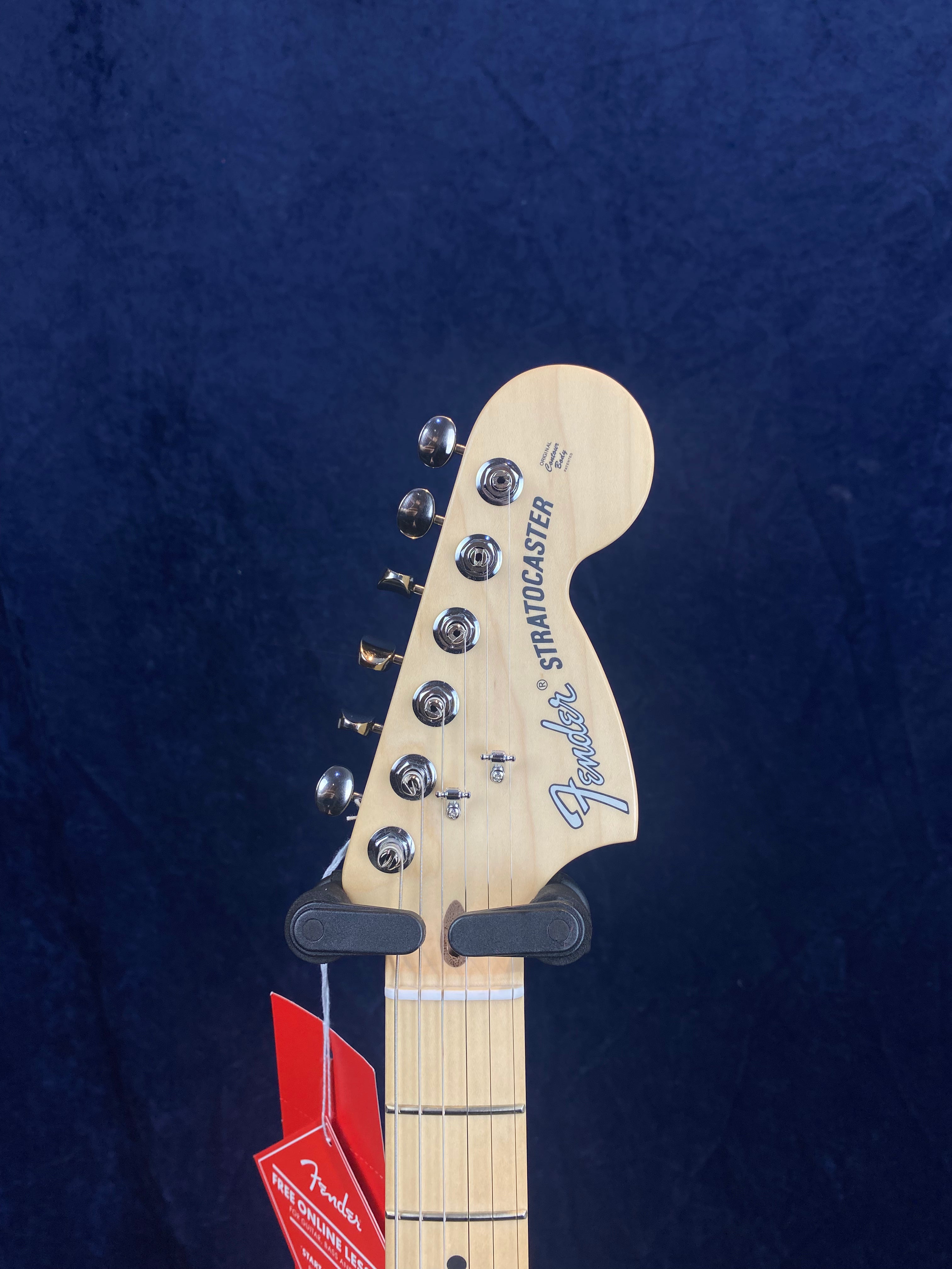 Fender Stratocaster electric guitar headstock with six tuning pegs, maple finish, and a red tag hanging from the neck.