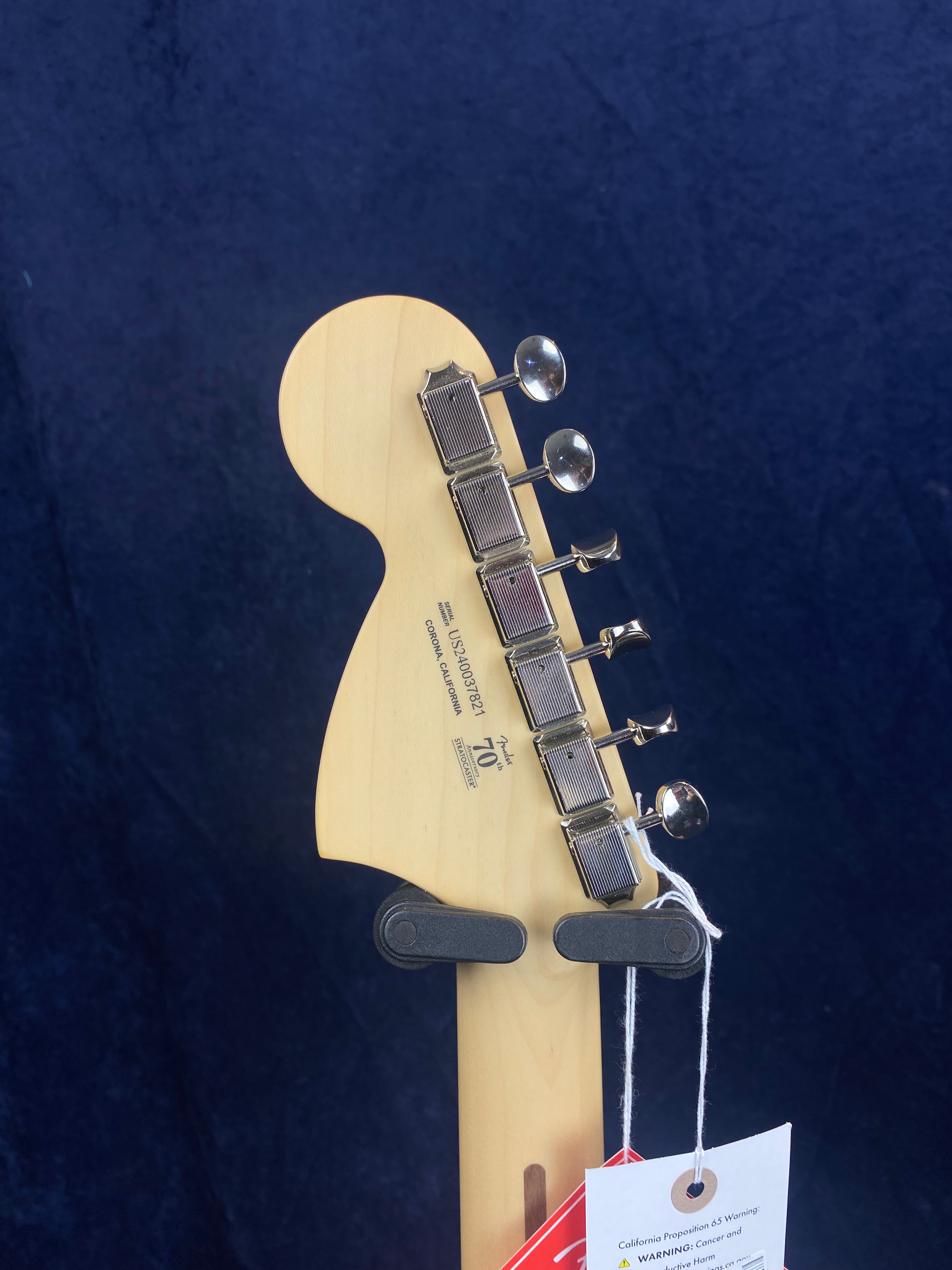 Light wood electric guitar headstock with six vintage-style tuning pegs, anniversary logo, and attached product tags.
