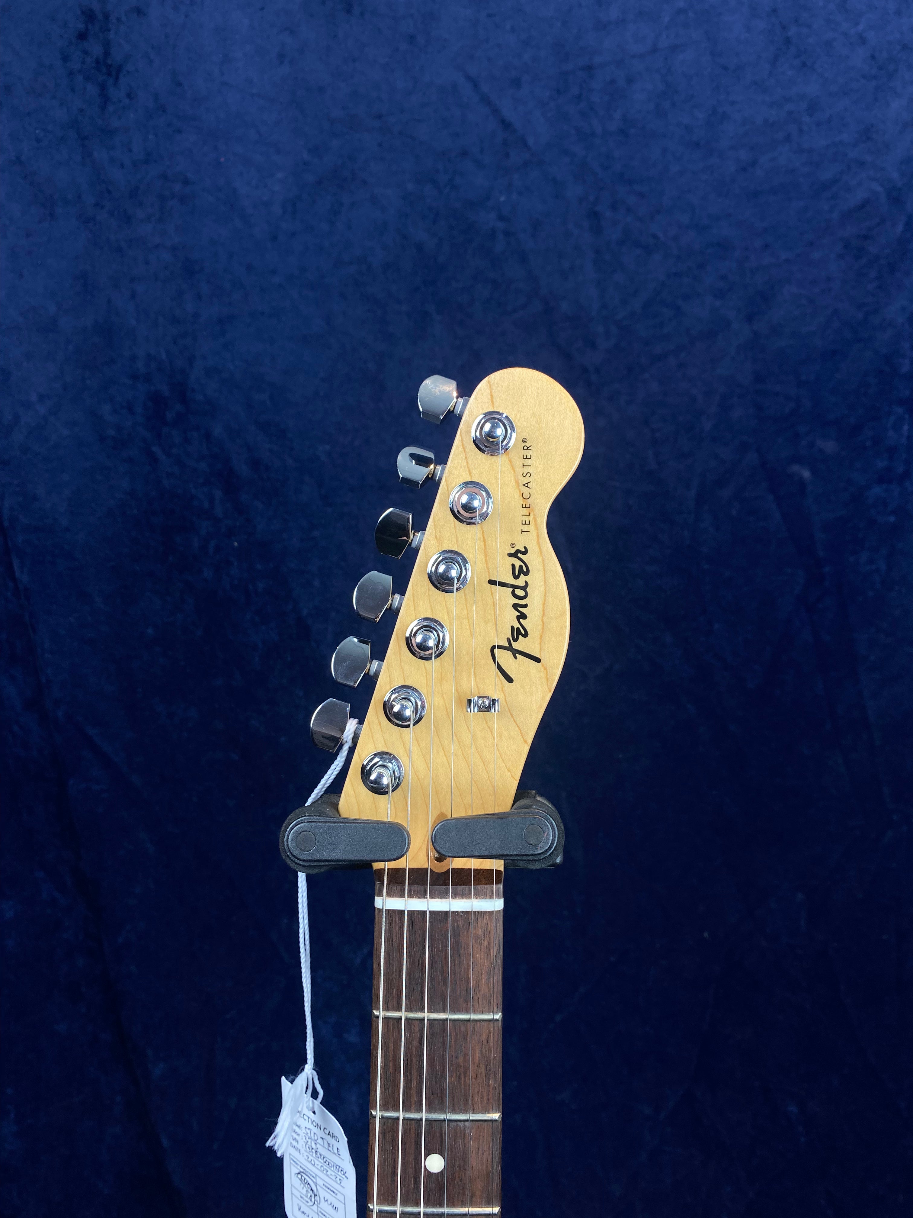 Light wood Fender Telecaster electric guitar headstock with six chrome tuning pegs, dark fretboard, and a white tag hanging from a string.