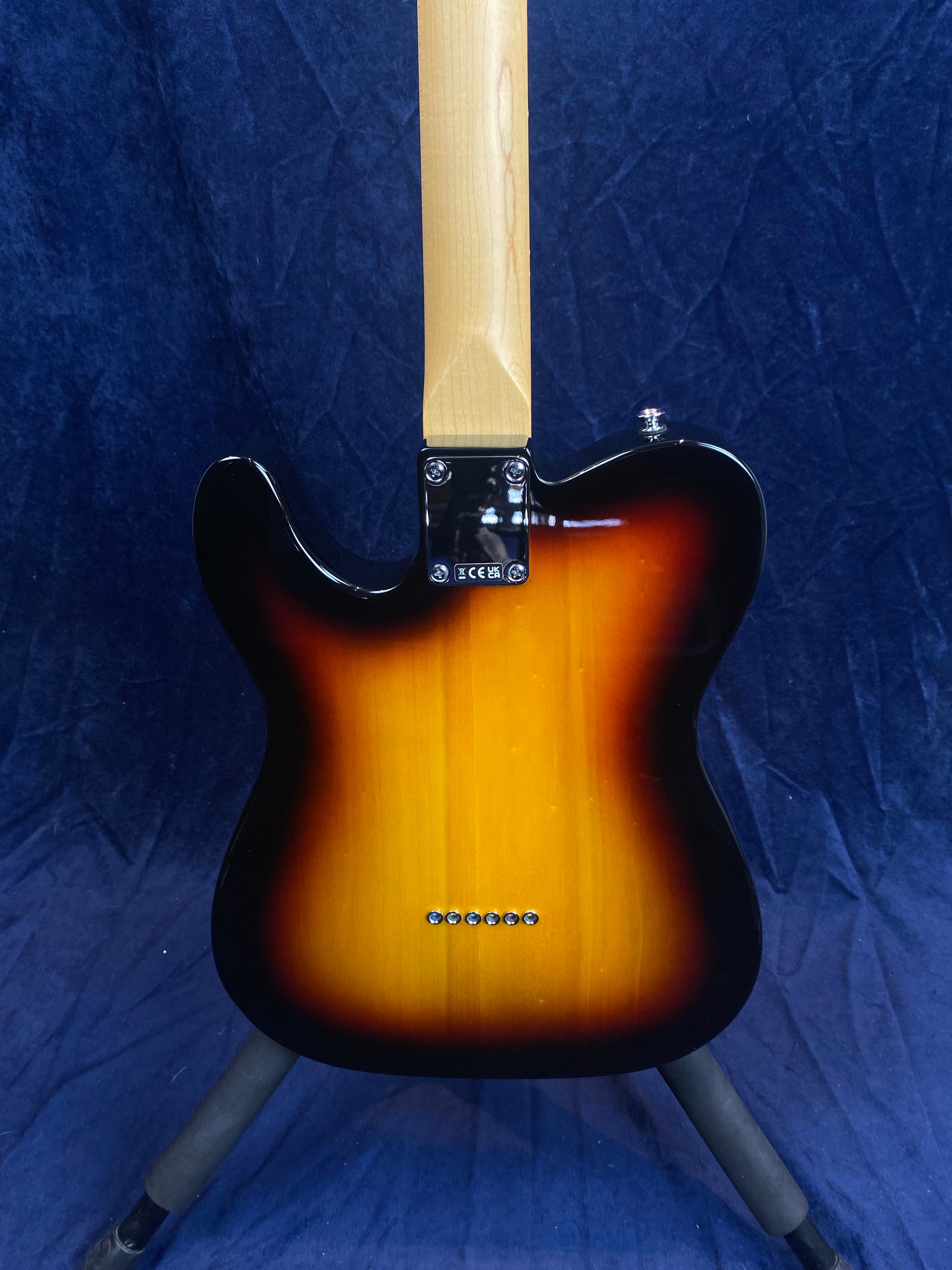 Sunburst finish electric guitar shown from the back, maple neck, six string ferrules in a row on the lower body, placed on a stand.