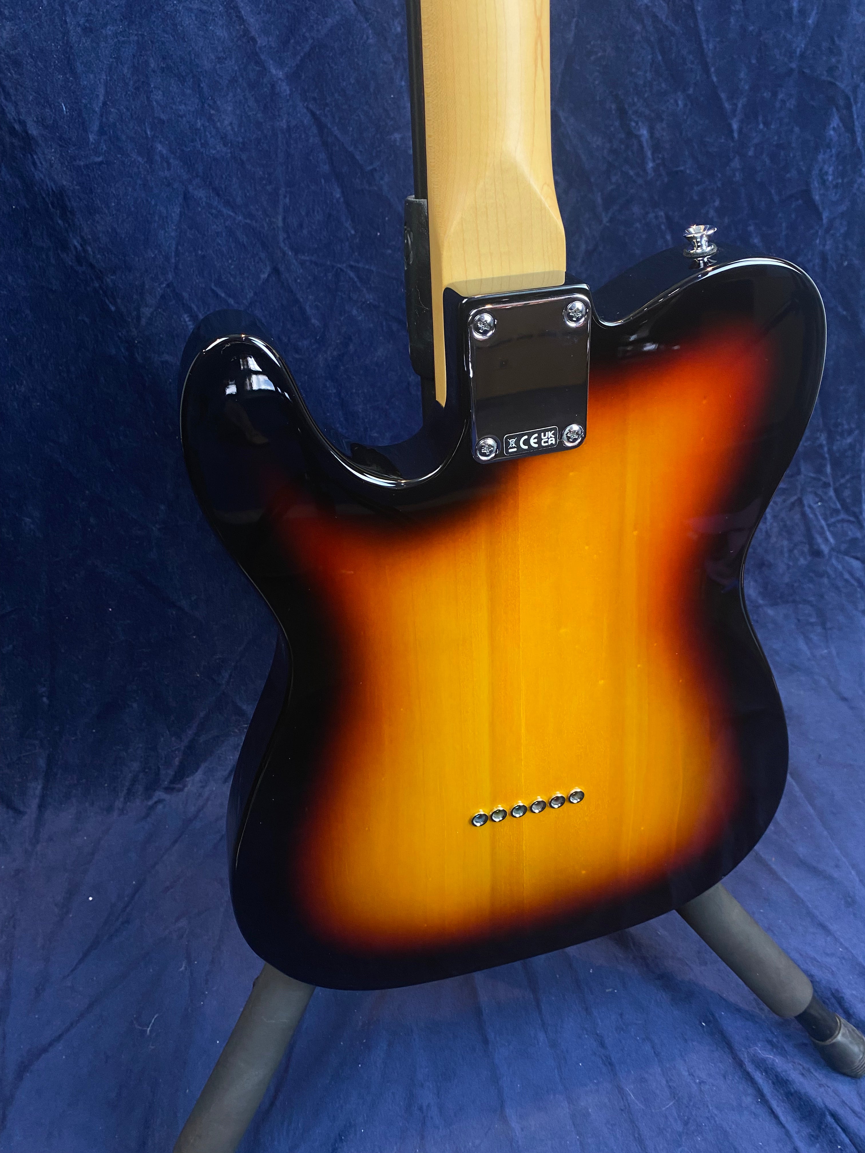 Back of a sunburst-finish electric guitar on a stand, showing the neck joint with four screws and six string ferrules in a straight line.