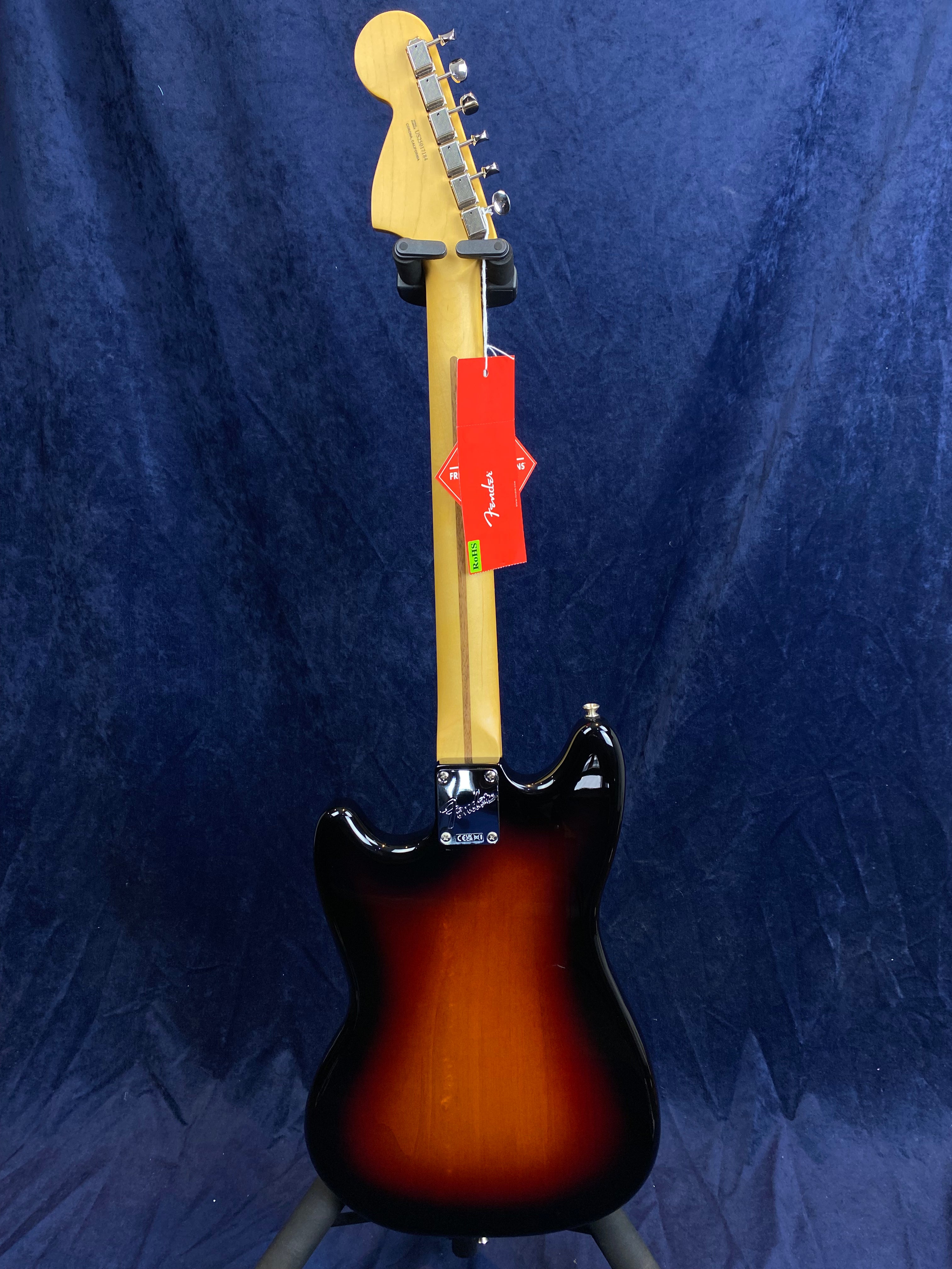 Sunburst finish electric guitar shown from the back, maple neck, metal tuners, and a red Fender tag hanging from the headstock.