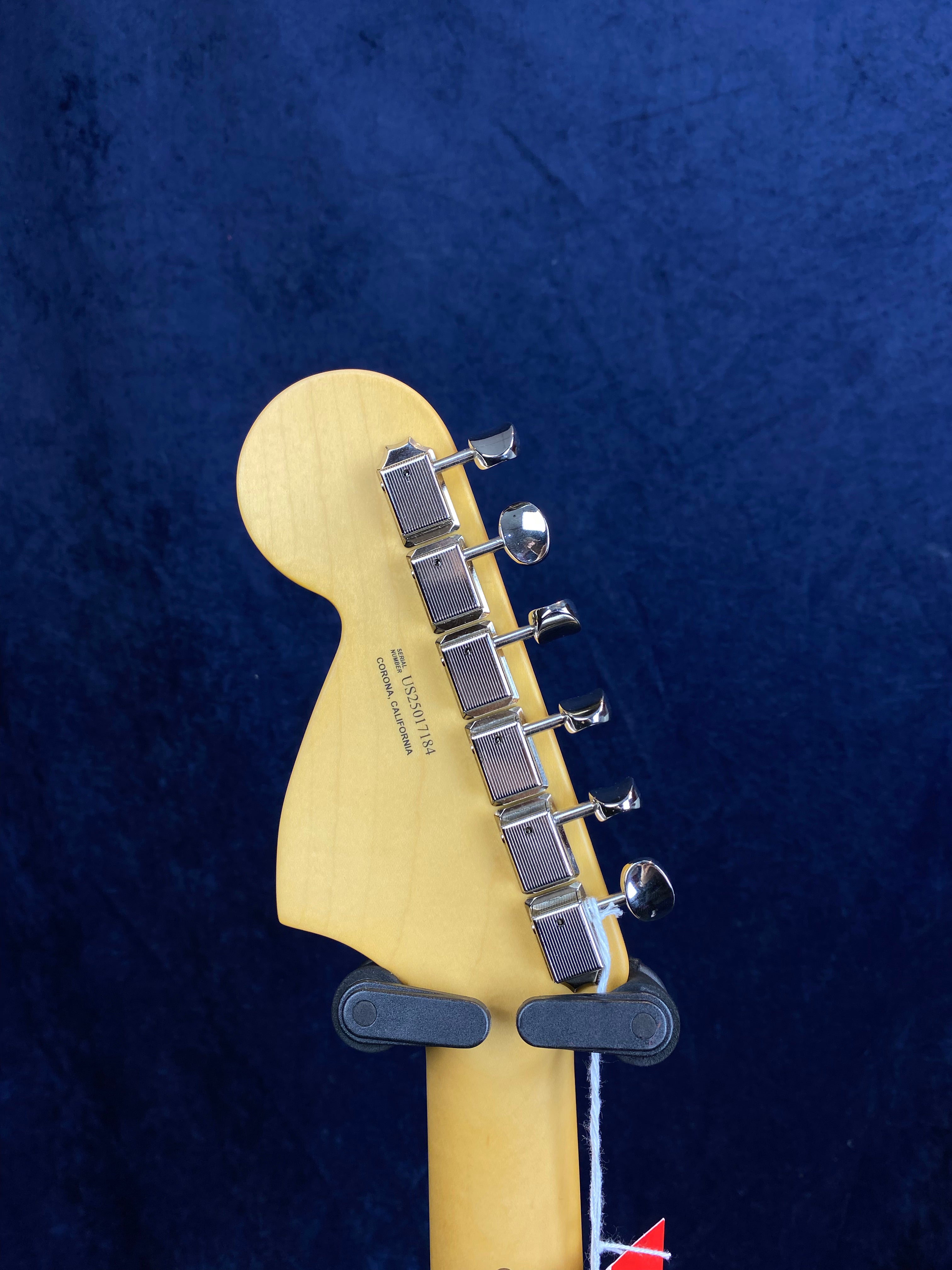 Electric guitar headstock in natural wood finish with six chrome tuning pegs, viewed against a dark blue background.
