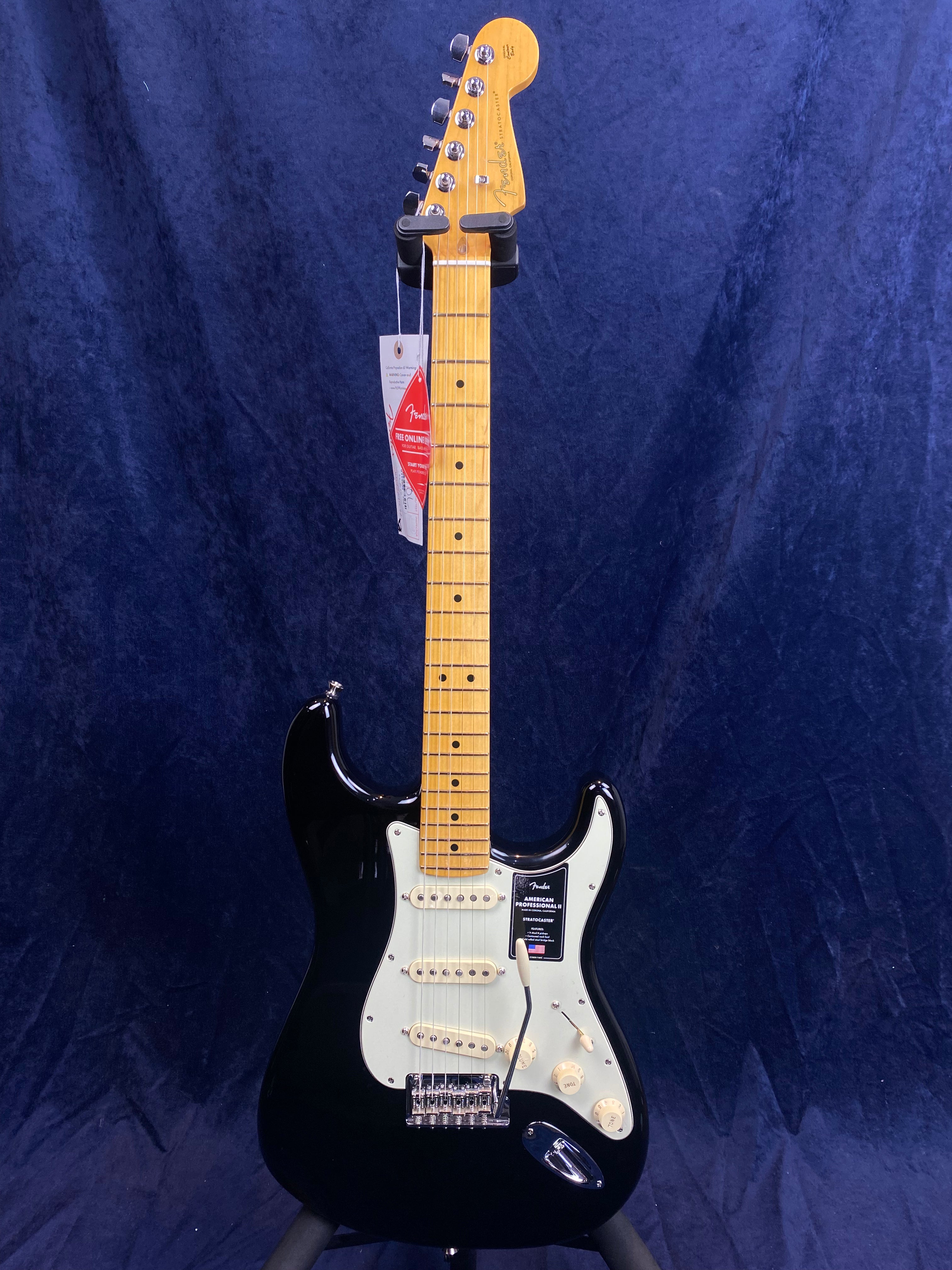 Black electric guitar with a light-colored pickguard, maple neck, and three single-coil pickups, displayed upright against a dark background.