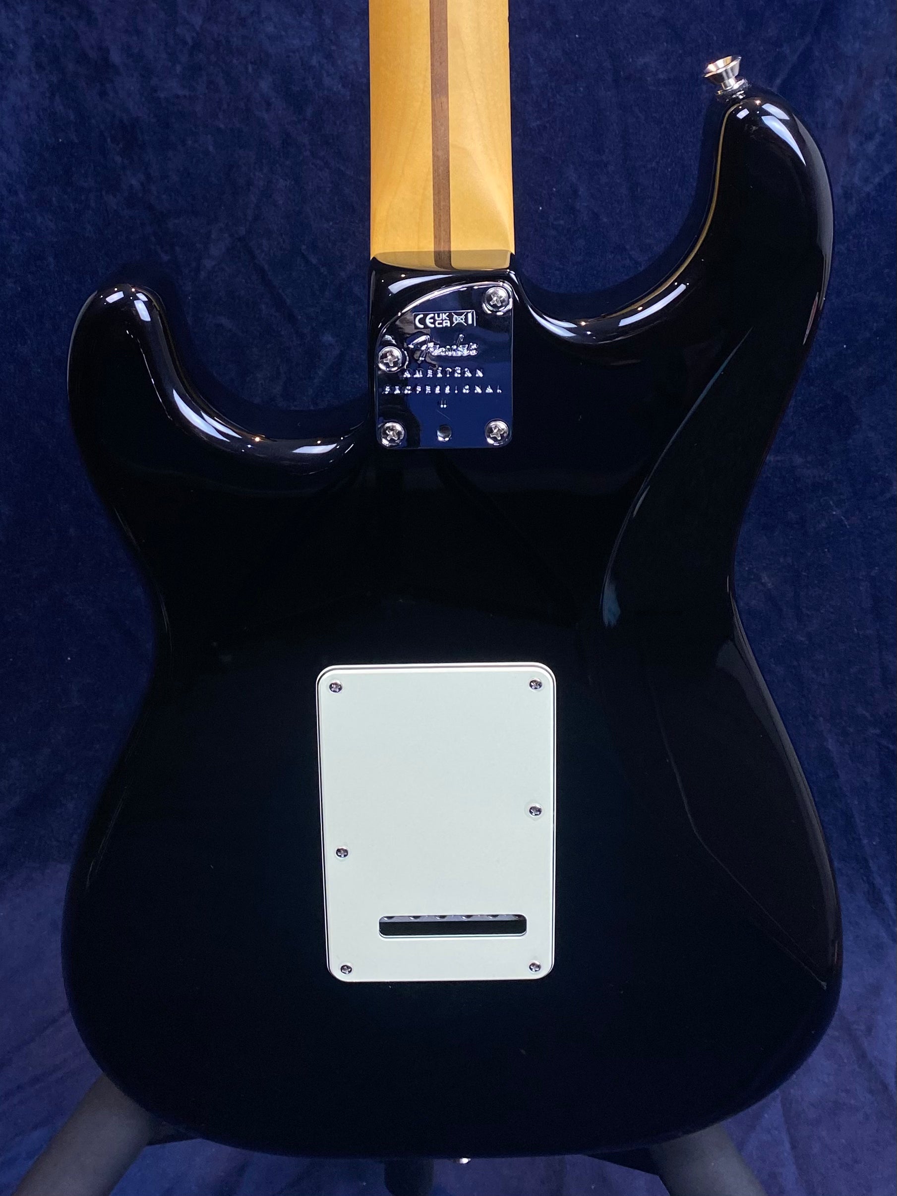Back view of a black electric guitar showing its maple neck, metal neck plate with Fender logo, and a rectangular white cover plate near the bottom.