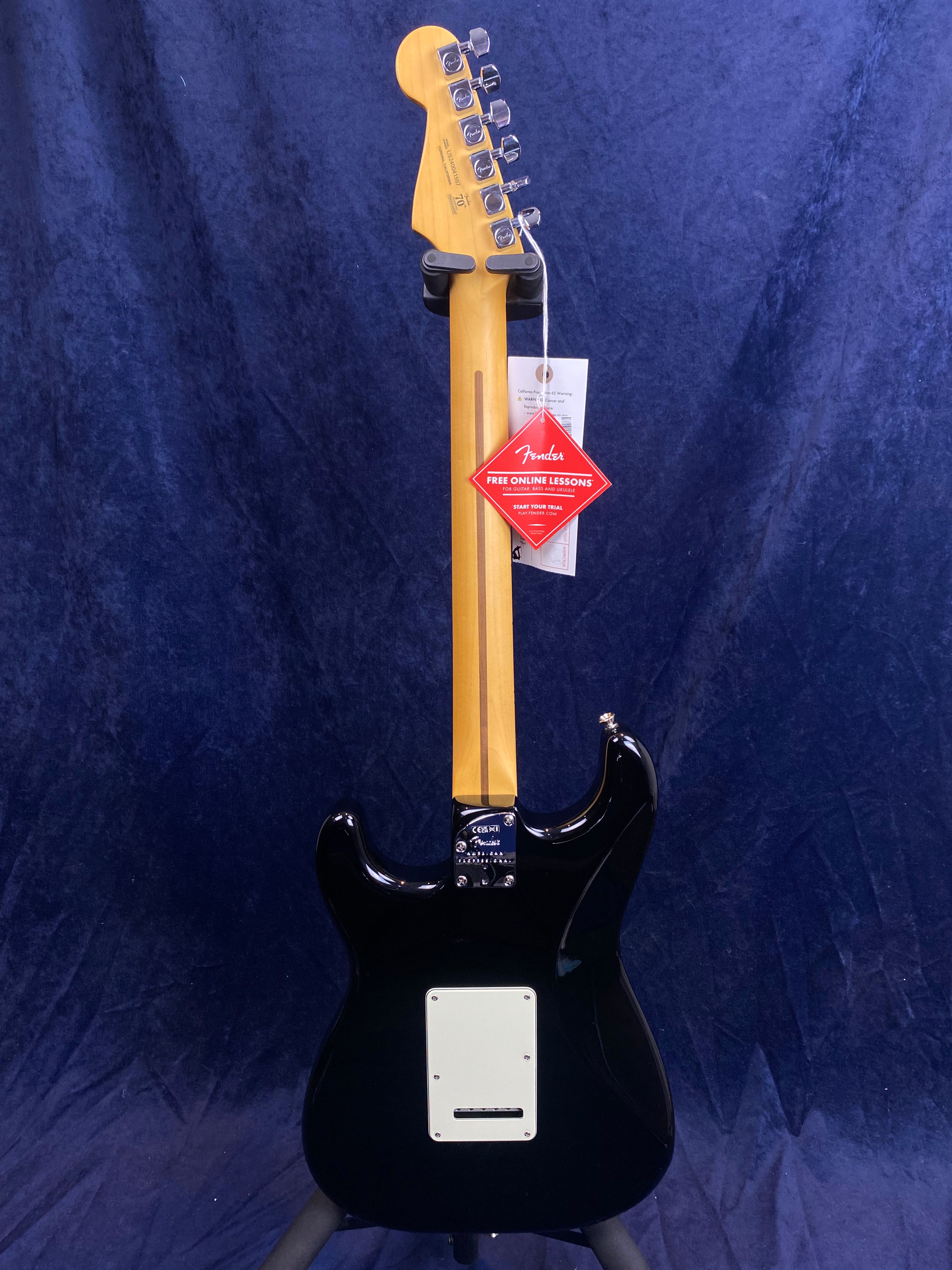 Black Fender electric guitar shown from the back with a maple neck, chrome tuners, and tags hanging from the headstock and tuning pegs.