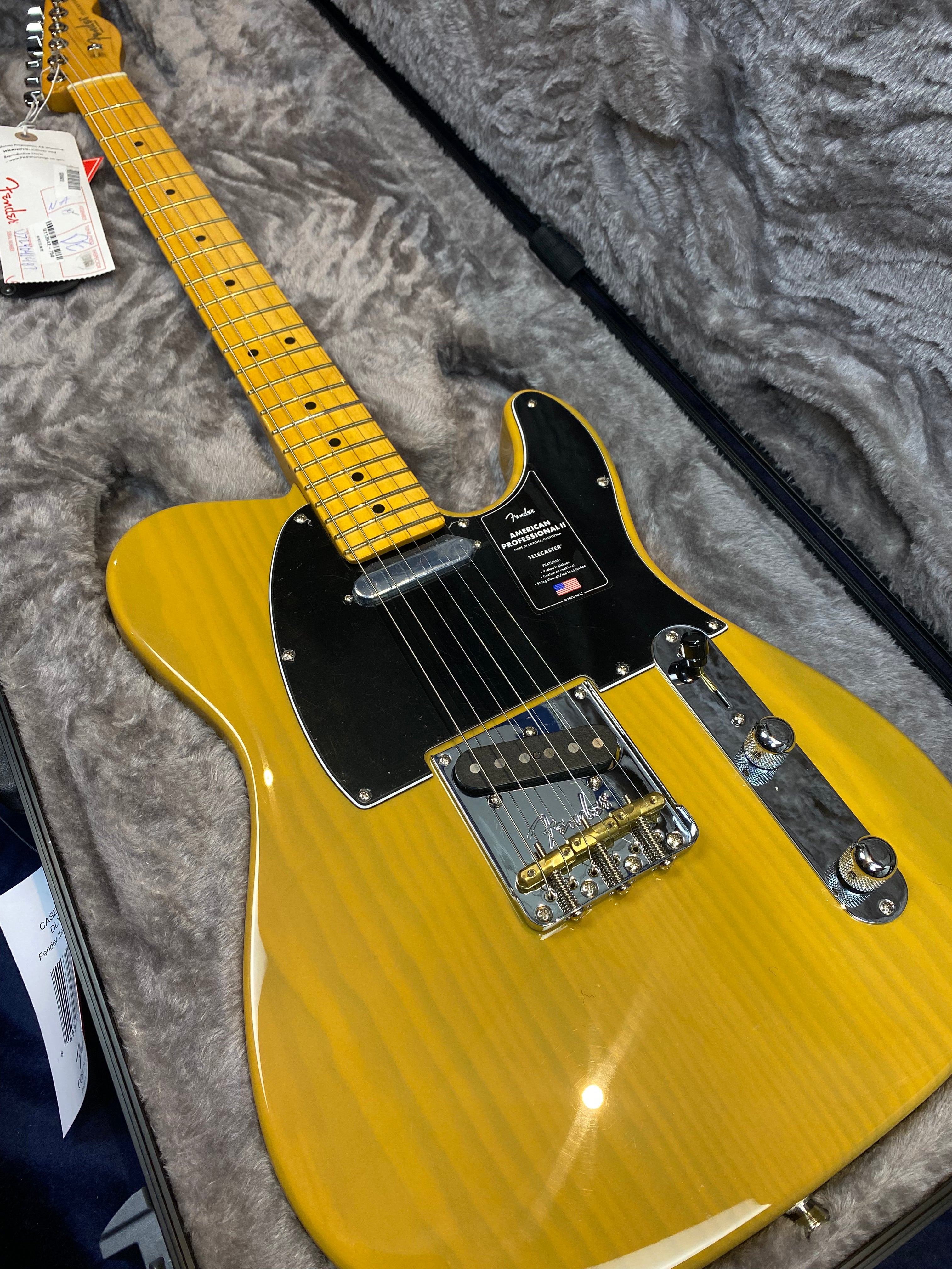 Yellow electric guitar with black pickguard, maple neck, metal bridge and knobs, resting in a gray lined hard case with Fender tags attached.