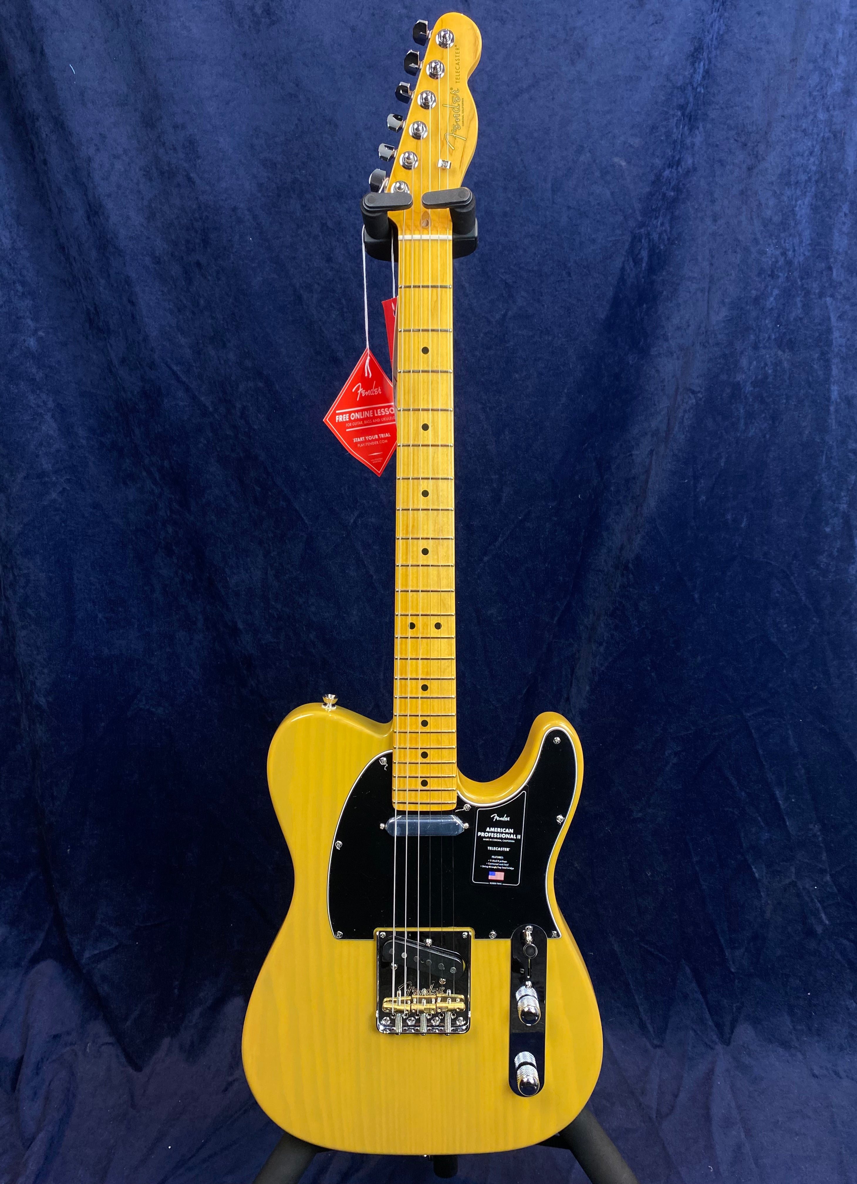 Yellow Fender electric guitar with black pickguard, maple neck, and two pickups stands upright against a dark blue background.