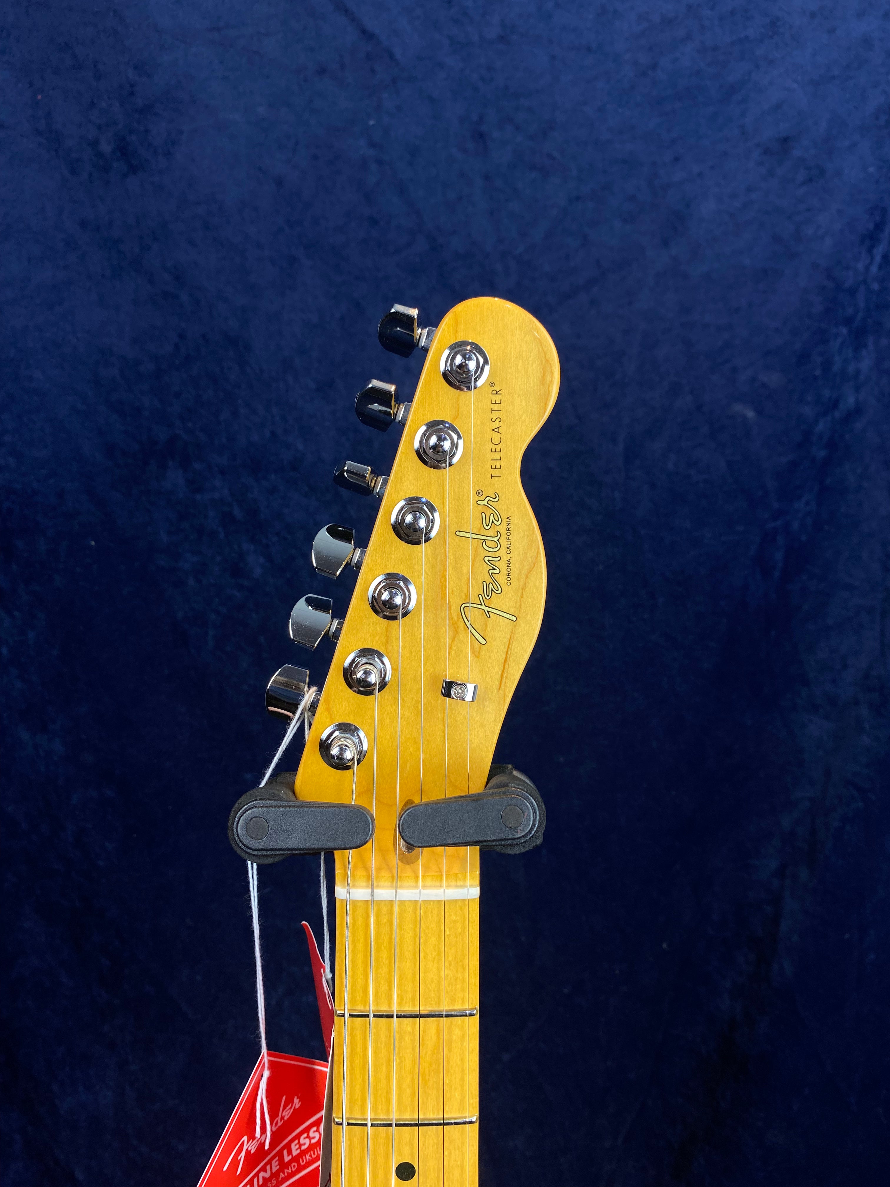 Fender Telecaster electric guitar headstock with six tuning pegs, maple neck, and a red Fender tag hanging below the nut.