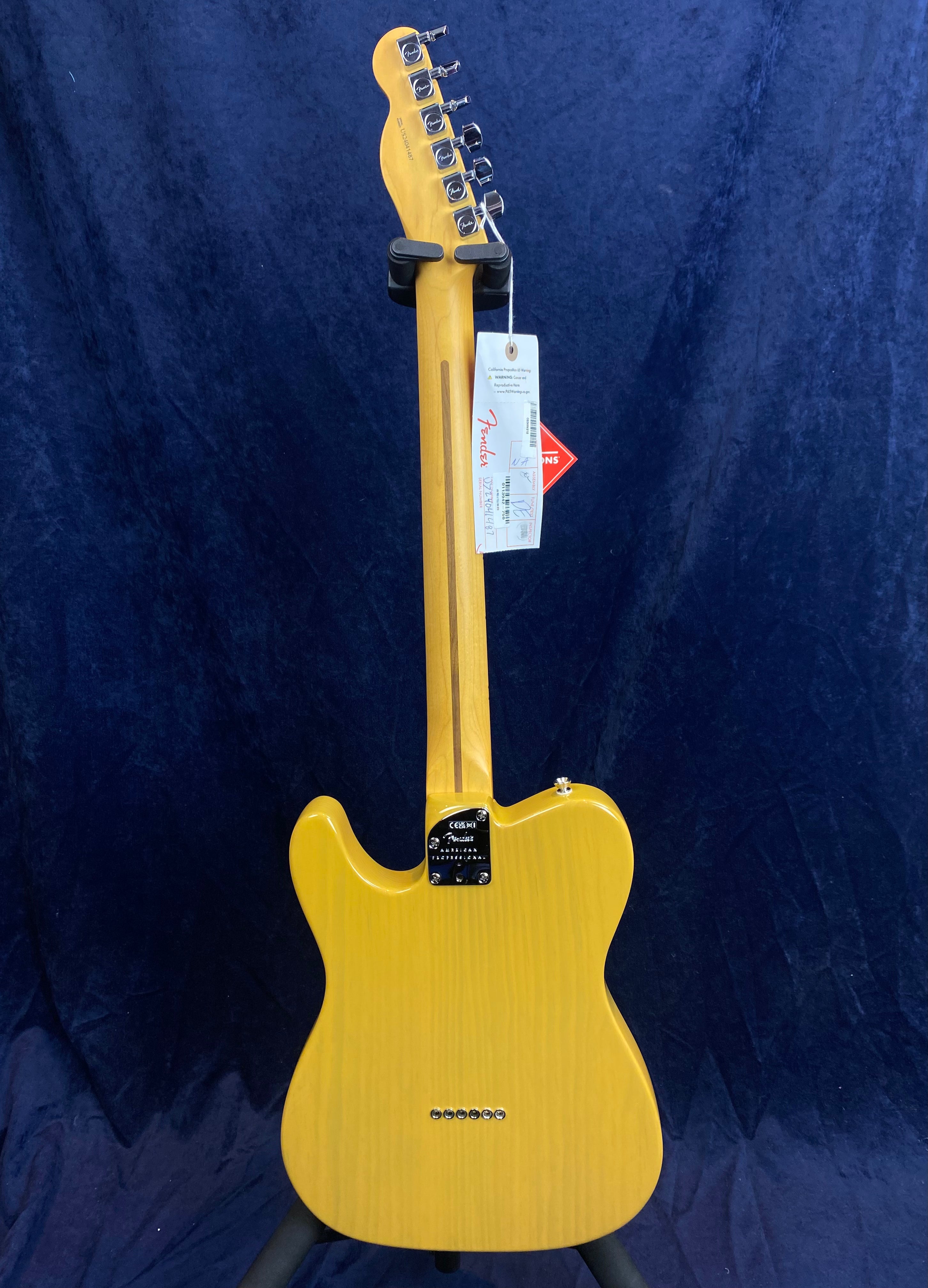 Yellow electric guitar shown from the back, displaying the neck, tuning pegs, and body grain, with Fender tags hanging from the headstock.