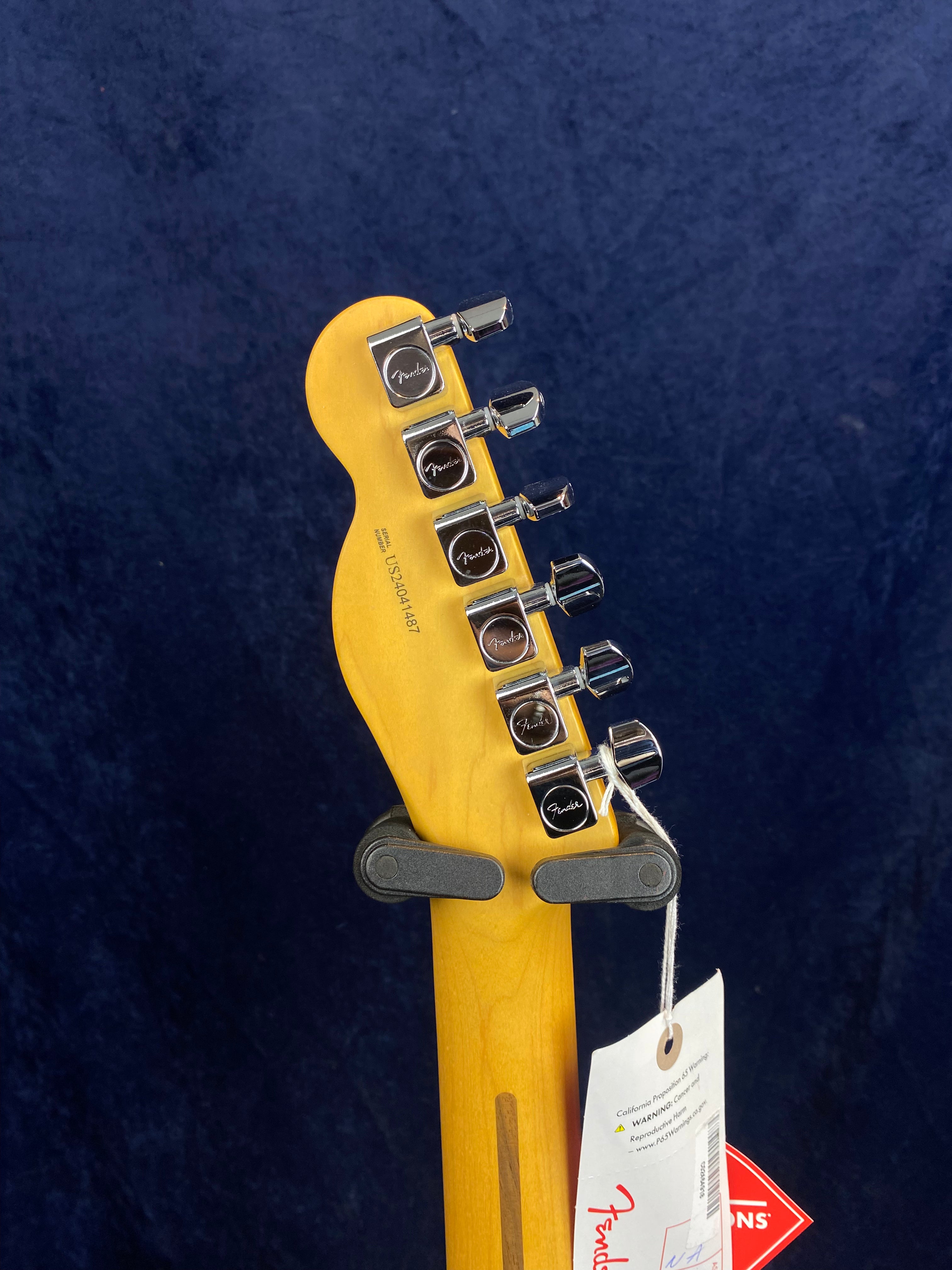 Back of a Fender electric guitar headstock, showing six chrome tuning pegs and hang tags attached to the neck.