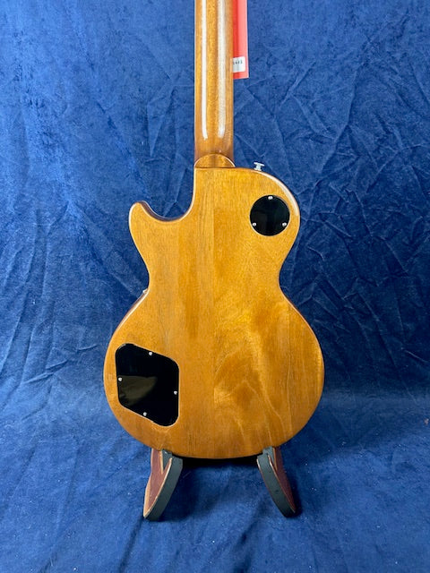 Natural wood finish electric guitar back view, showing two black plastic access panels and rounded single-cutaway body shape against a blue background.