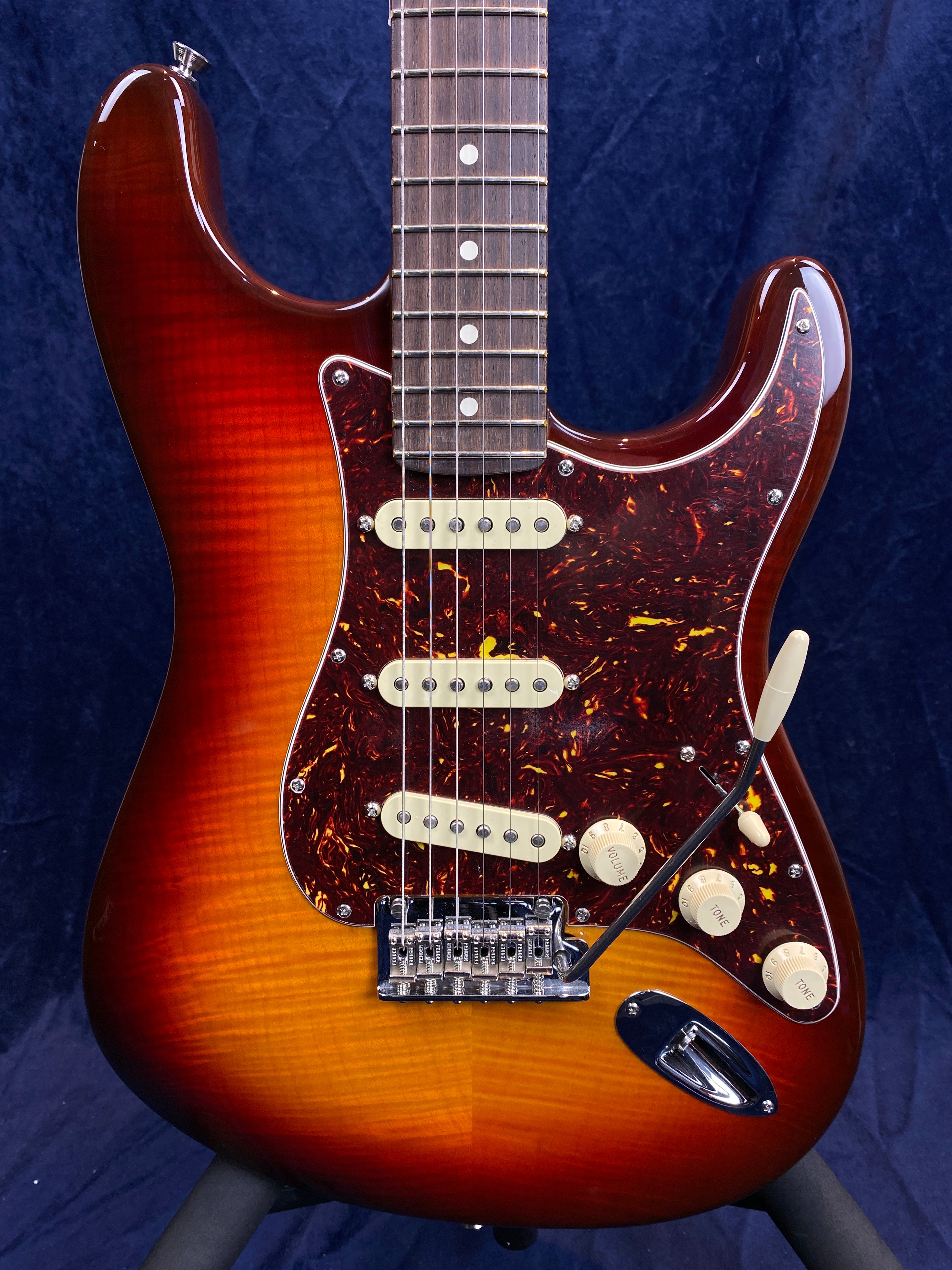Sunburst electric guitar with a tortoiseshell pickguard, three single coil pickups, five control knobs, and a whammy bar.