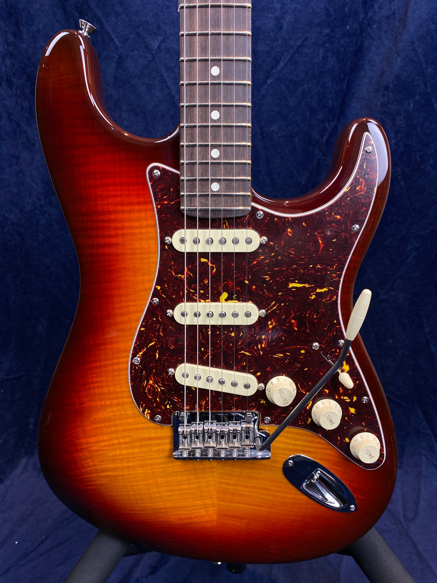 Sunburst electric guitar with a tortoiseshell pickguard, three single coil pickups, five control knobs, and a whammy bar.