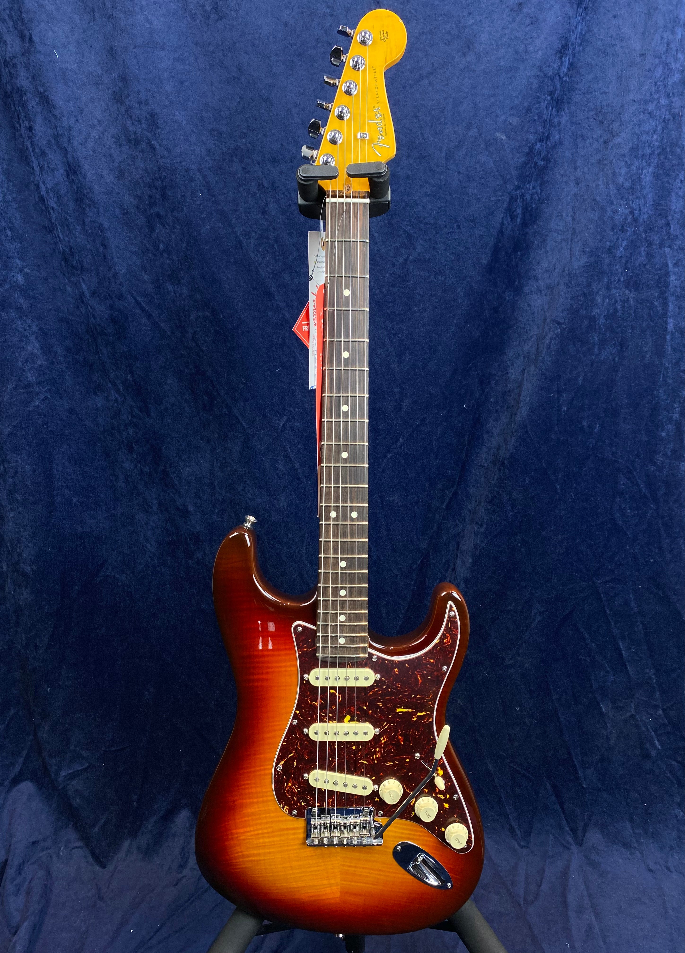 Sunburst Fender Stratocaster electric guitar with three single-coil pickups, white knobs, and a dark tortoiseshell pickguard against a dark blue background.