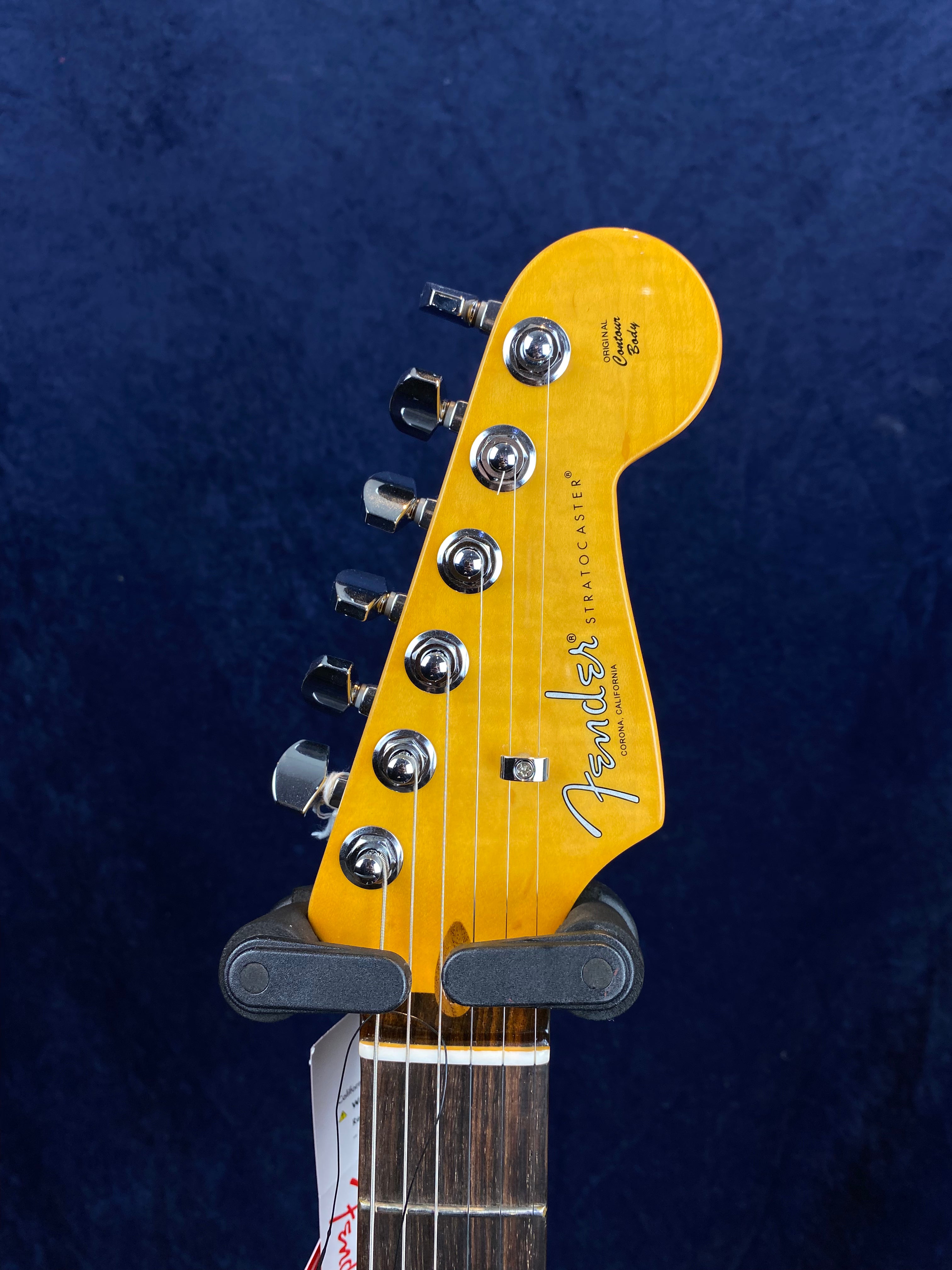 Yellow Fender Stratocaster electric guitar headstock with six tuning pegs, chrome hardware, and visible logo against a dark blue background.