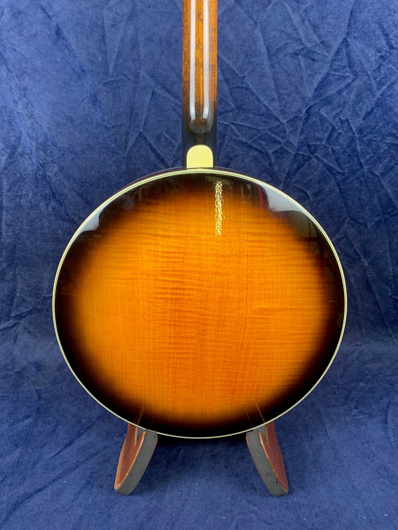 The back of a vintage mandolin with a glossy sunburst finish, rounded body, and wood grain visible, displayed upright on a stand against dark fabric.
