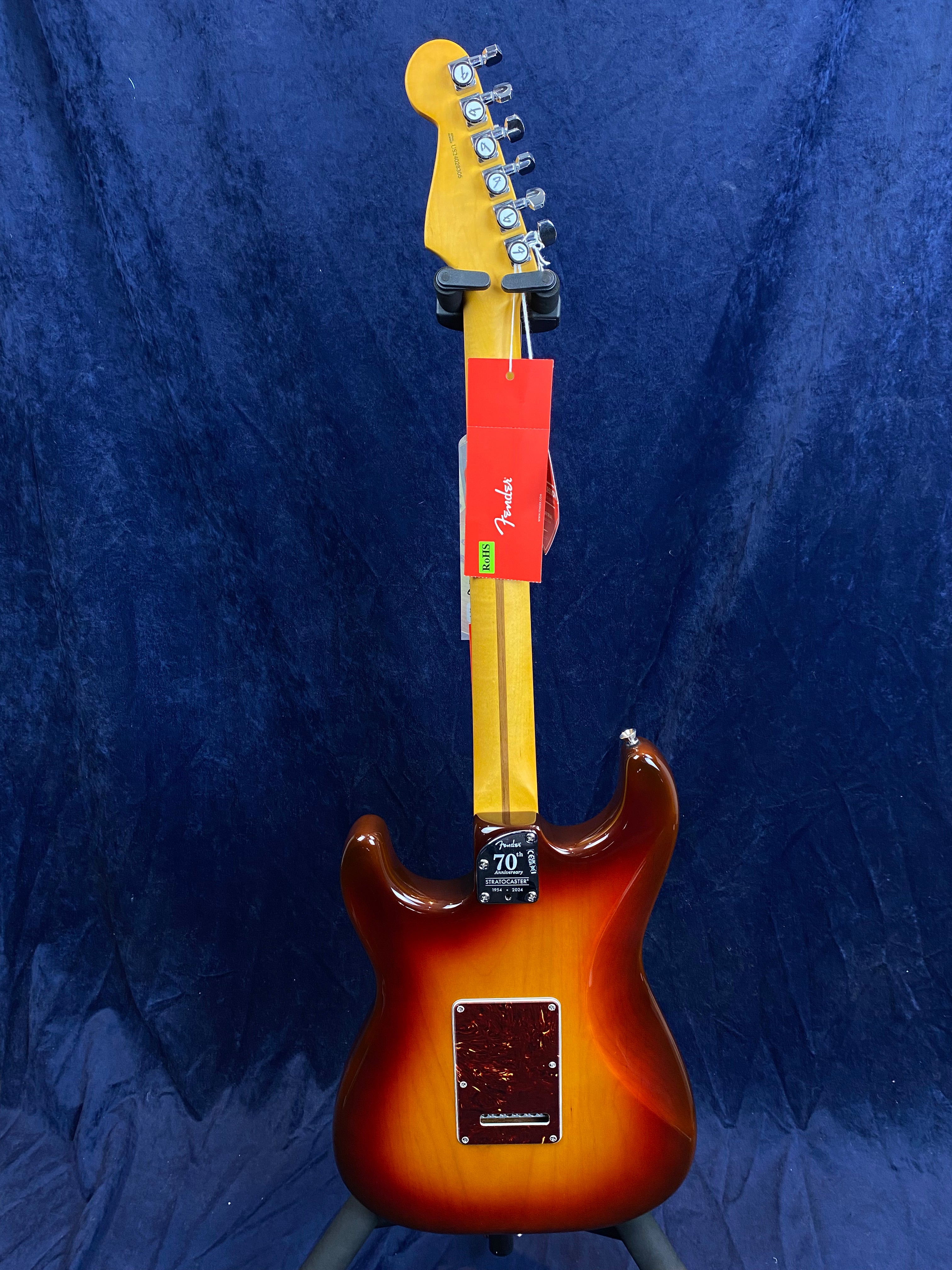 Sunburst Fender electric guitar shown from the back with a maple neck, chrome tuners, and red Fender tag attached to the headstock.