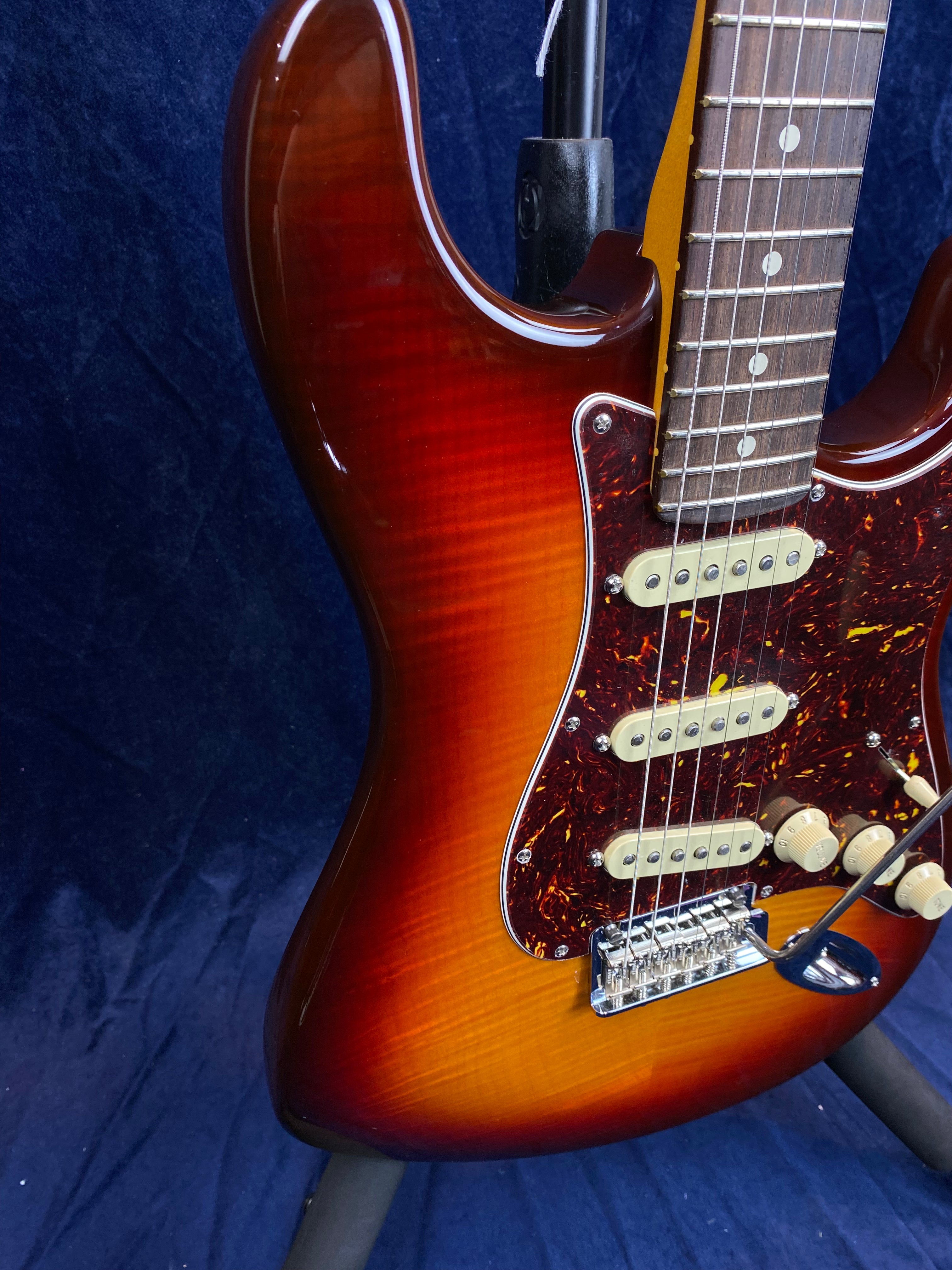 Sunburst electric guitar with a glossy finish, three cream single-coil pickups, tortoiseshell pickguard, and white control knobs.