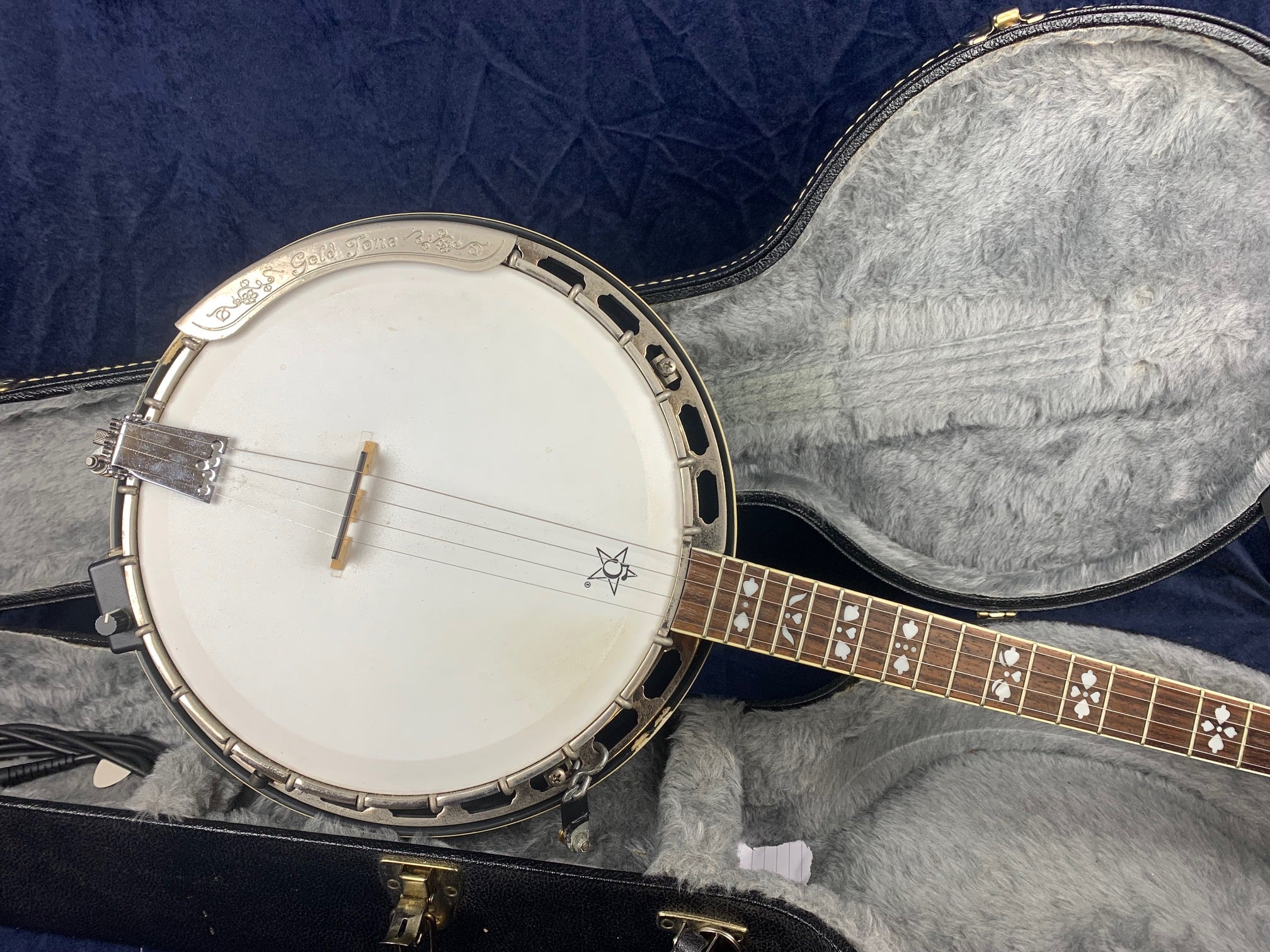 Pre-owned Gold Tone banjo with a white drumhead, five strings, decorative inlays on the fretboard, and a hard shell case lined with gray plush fabric.