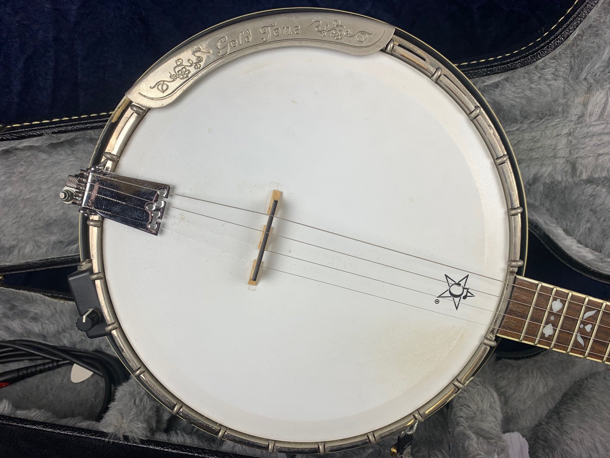 Close-up of a vintage Gold Tone banjo head showing strings, bridge, and a star design near the neck; instrument rests in a lined hard case.