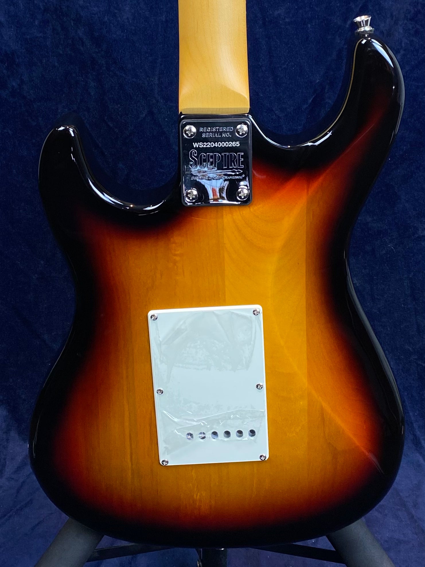 Sunburst electric guitar back with a white plastic cover plate held by screws, chrome neck plate engraved with “Sceptire” and serial number.