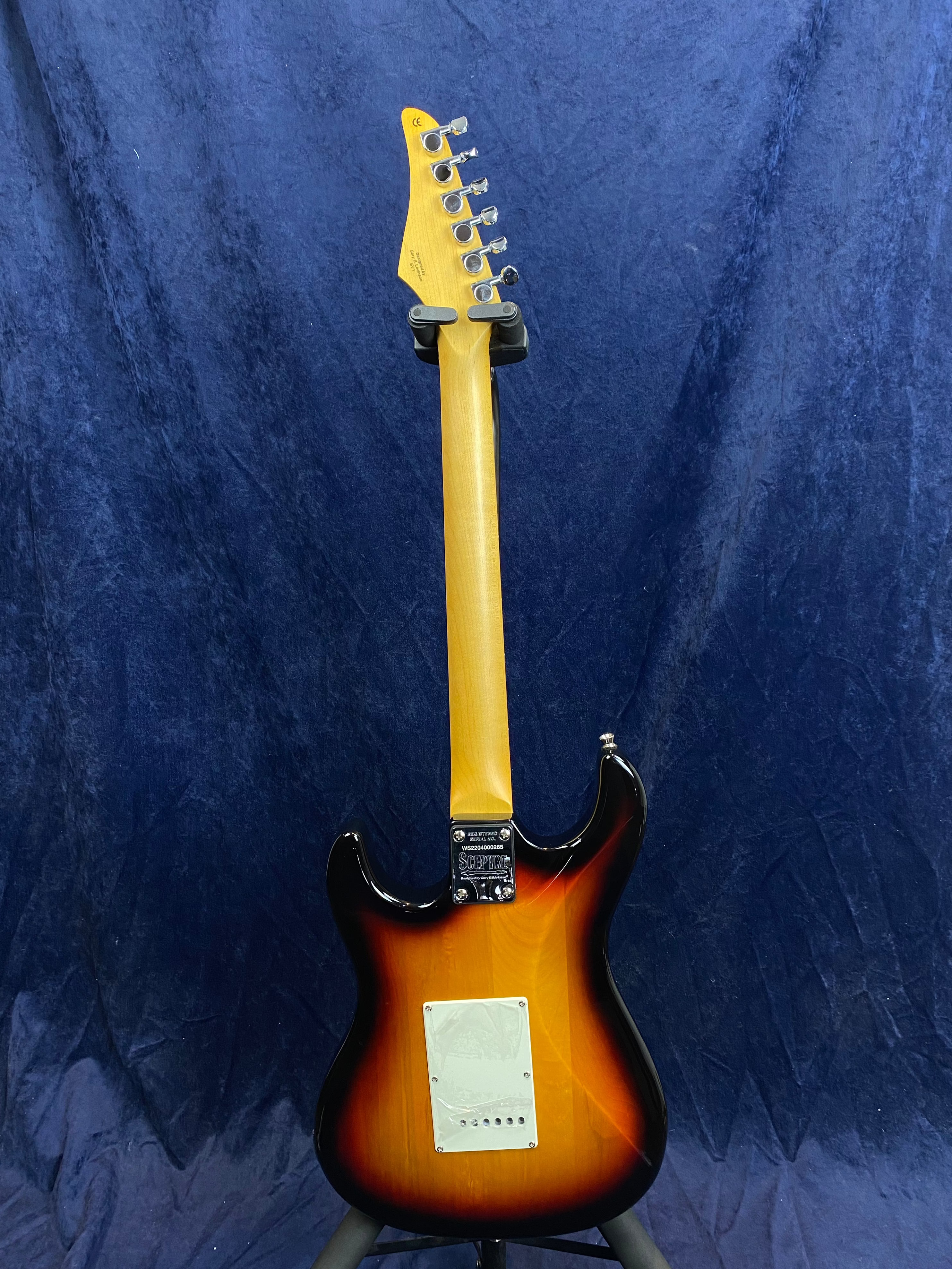 Sunburst electric guitar seen from the back, showing a light wood neck, six tuning pegs, and a white plastic cover on the body.