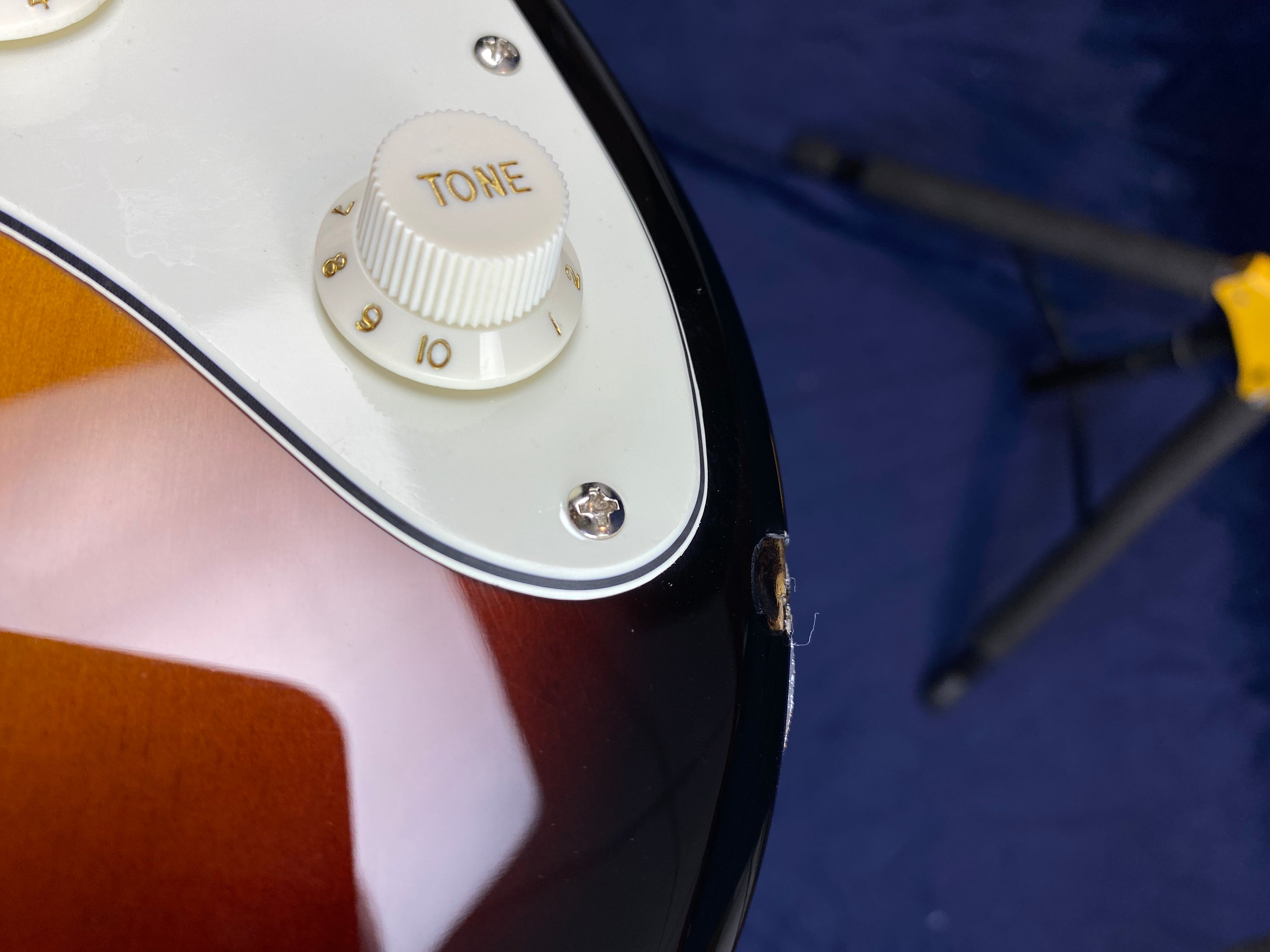 Electric guitar body with a white tone knob and visible edge damage exposing wood near the black finish.