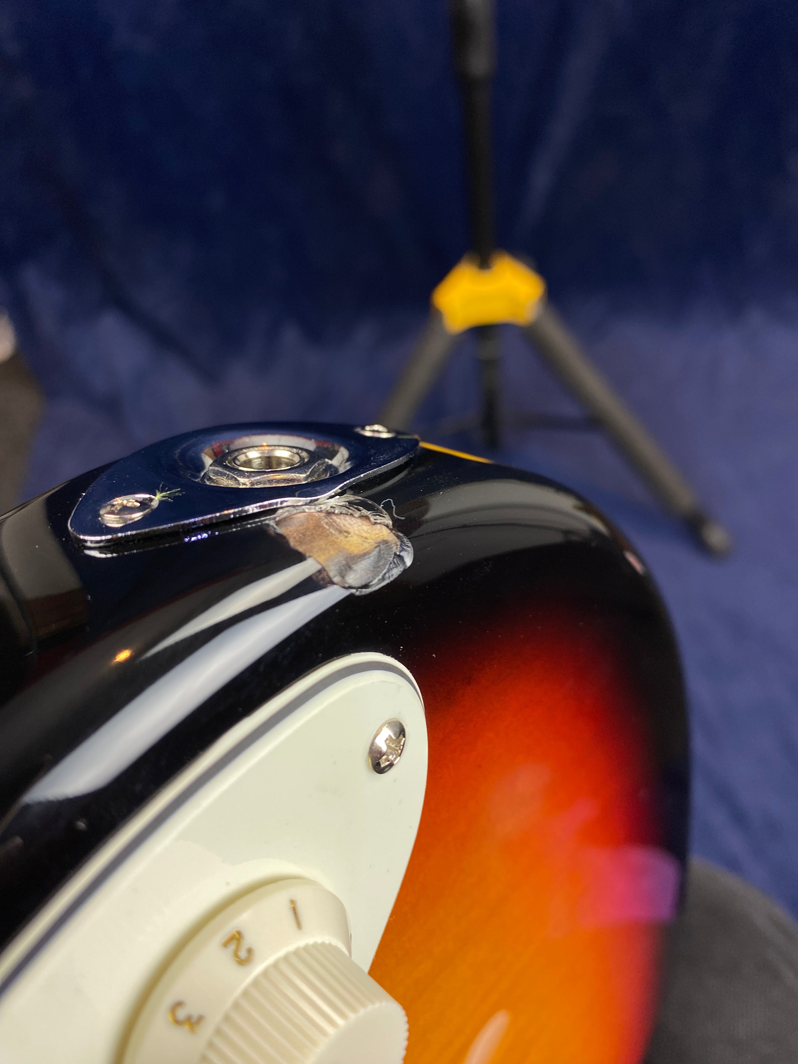 Electric guitar body with sunburst finish has a large chip and exposed wood near the input jack. White tone control knob numbered 1 to 3 is visible.