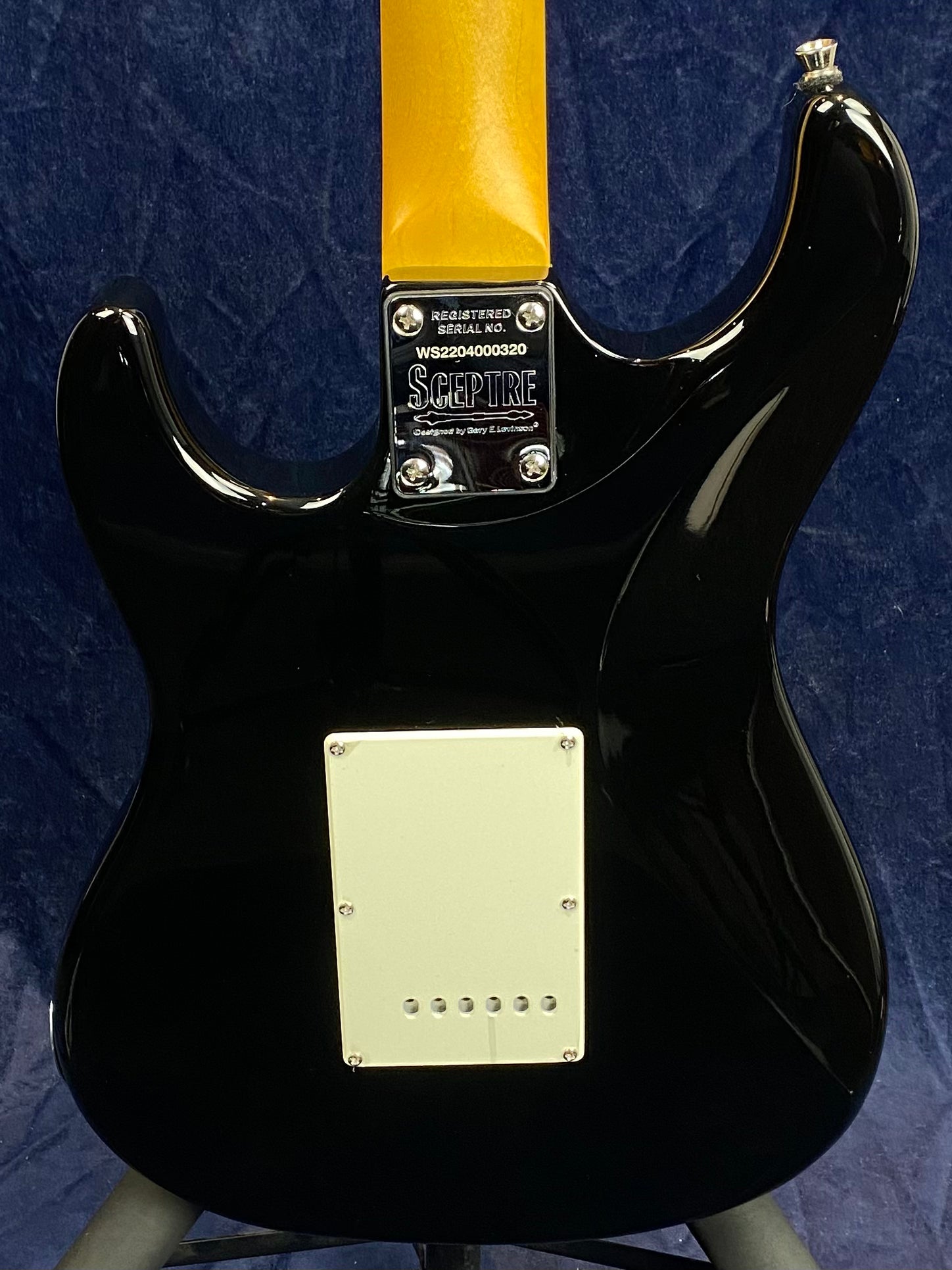 Black Sceptre electric guitar viewed from the back, showing a cream cover plate and a metal neck plate with serial number and logo.