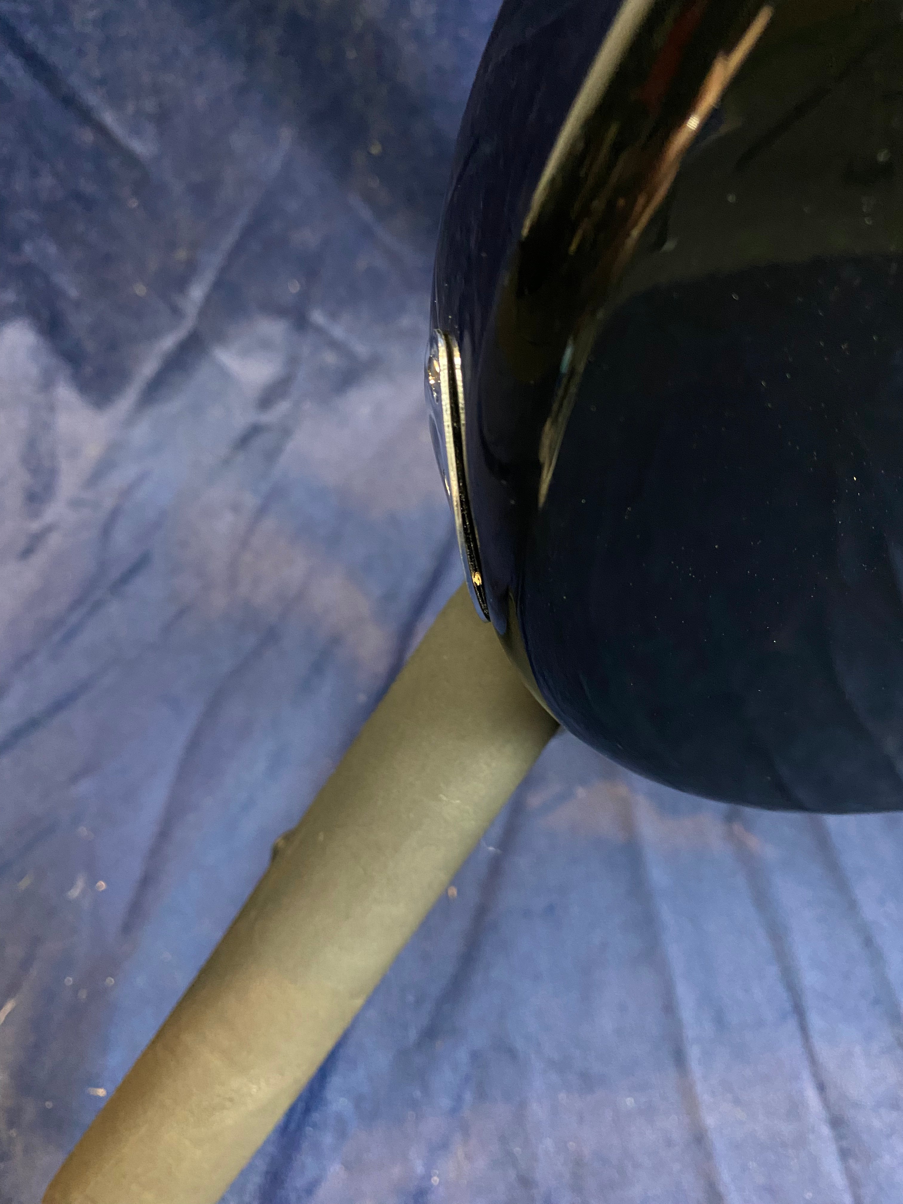 Part of a glossy black electric guitar body rests on a padded stand, against a blue fabric background.