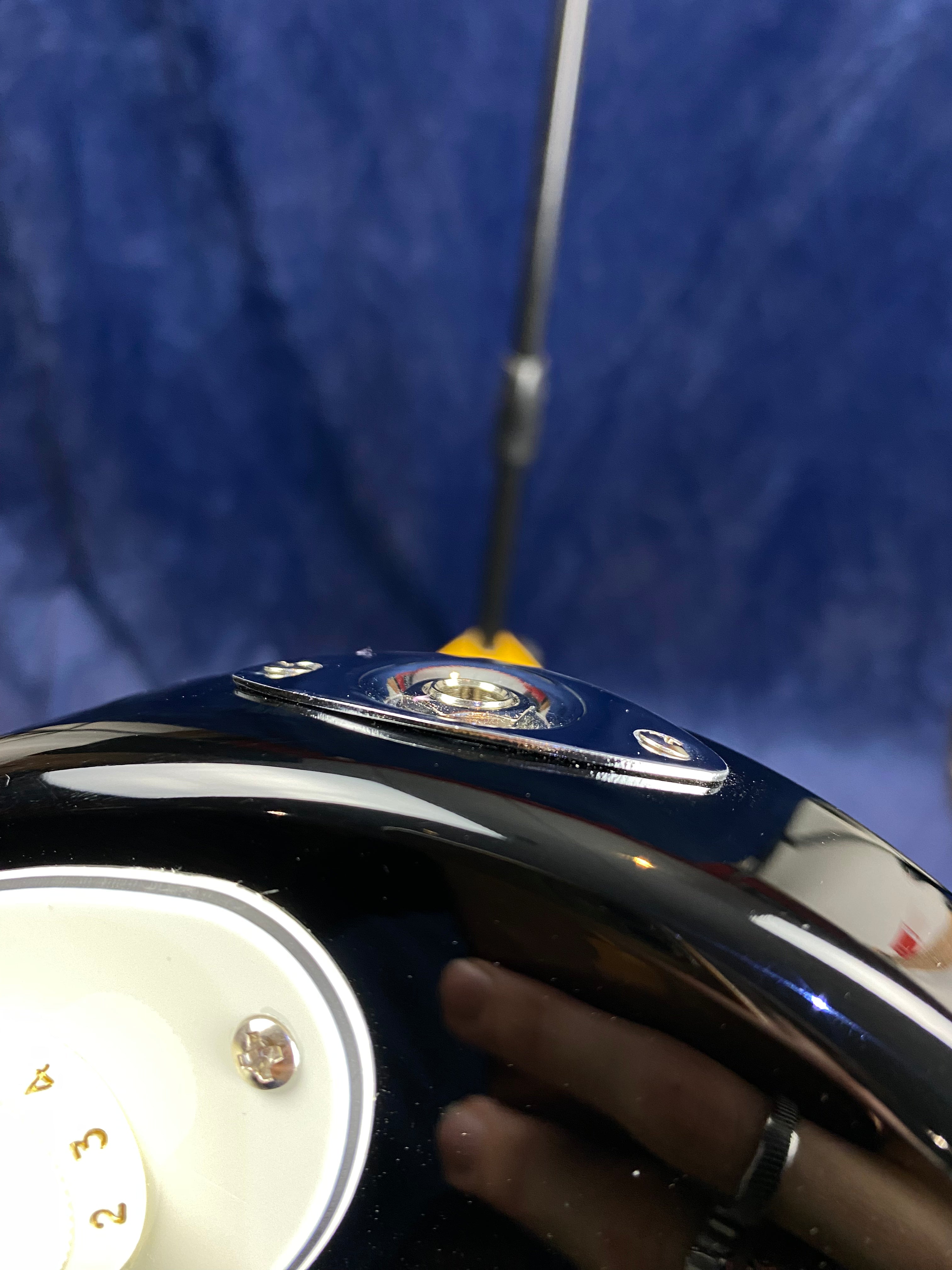 Close-up of an electric guitar's input jack and part of a white control knob numbered 1 to 4 against a blurred blue background.