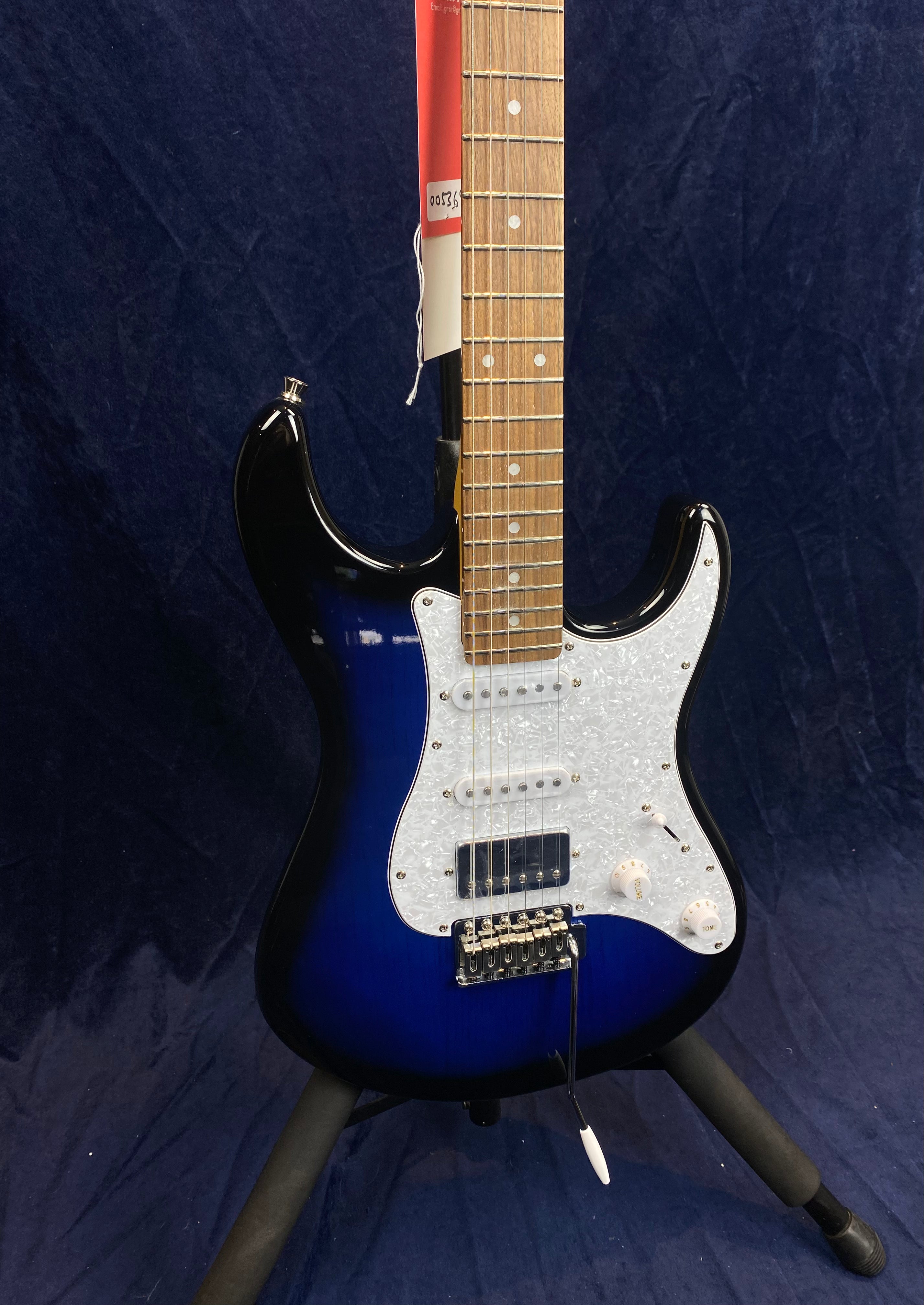Blue and black electric guitar with a white pearloid pickguard, three pickups, two control knobs, and a whammy bar, standing on a tripod stand.