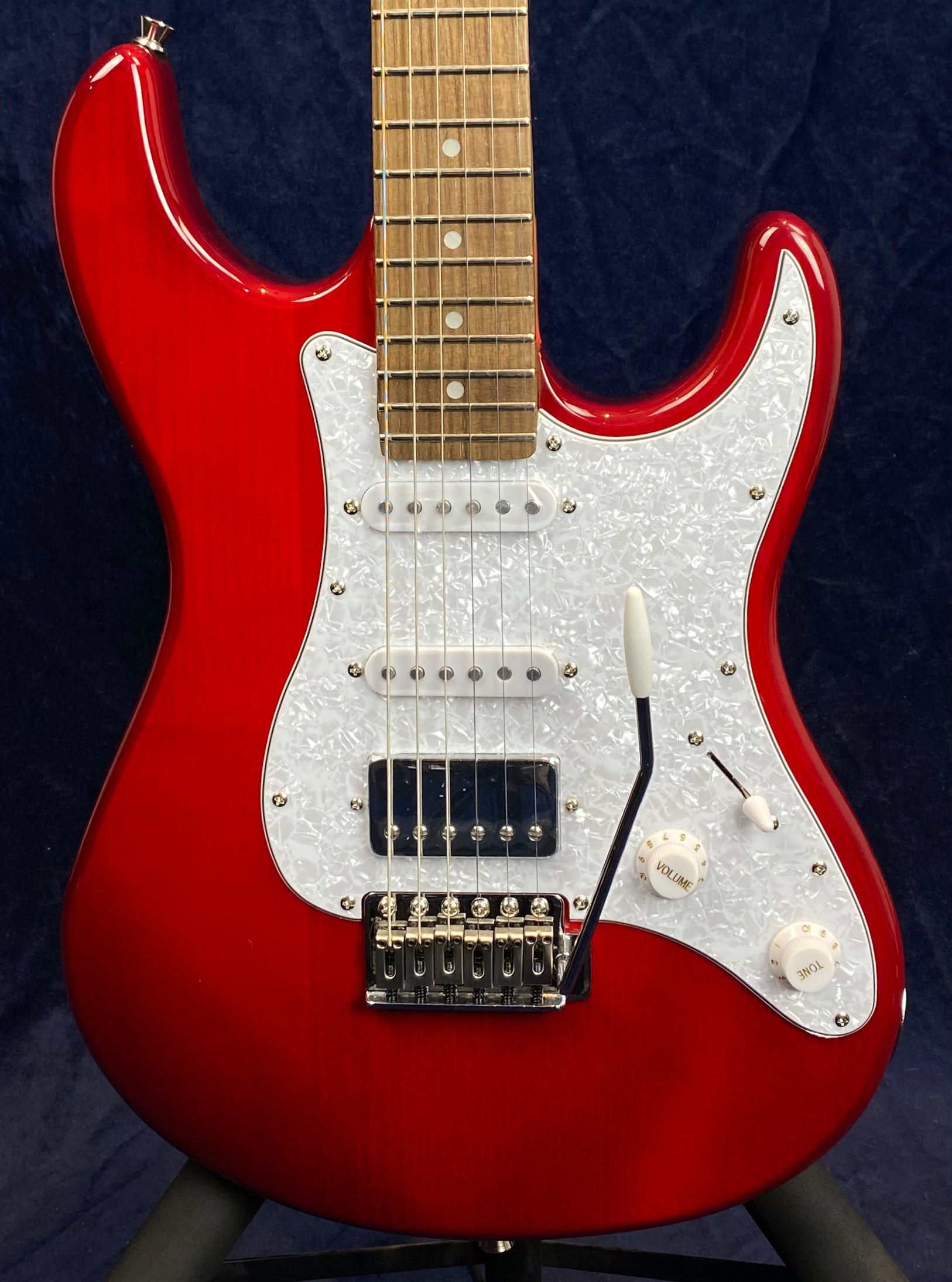 Red electric guitar with a white pearloid pickguard, three pickups, volume and tone knobs, and a whammy bar, shown from neck to bridge.