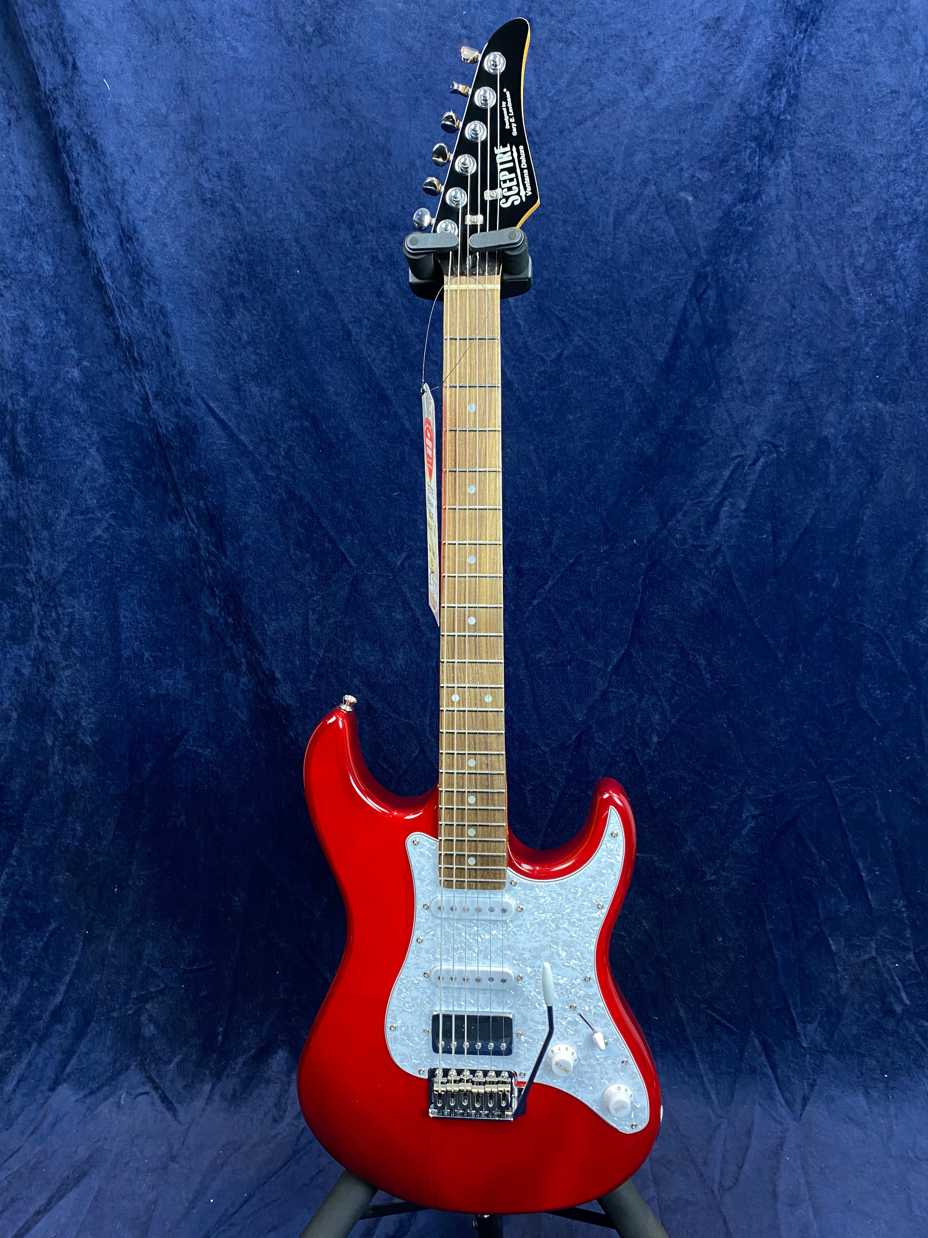 Glossy red electric guitar with a white pickguard, maple neck, six tuning pegs, and three pickups, set against a dark blue background.