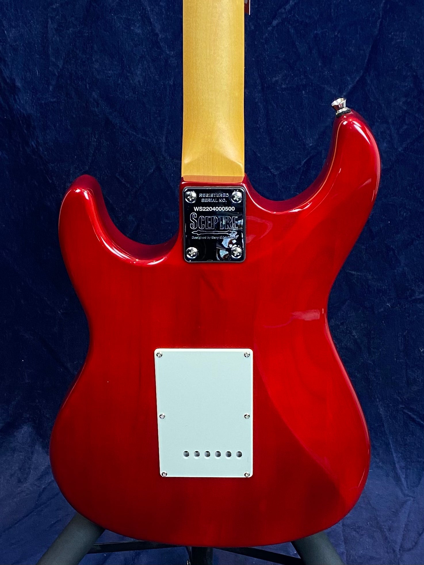 Glossy red electric guitar back with a natural wood neck, white electronics cover, and a metal neck plate engraved with "Sceptre" and serial number.