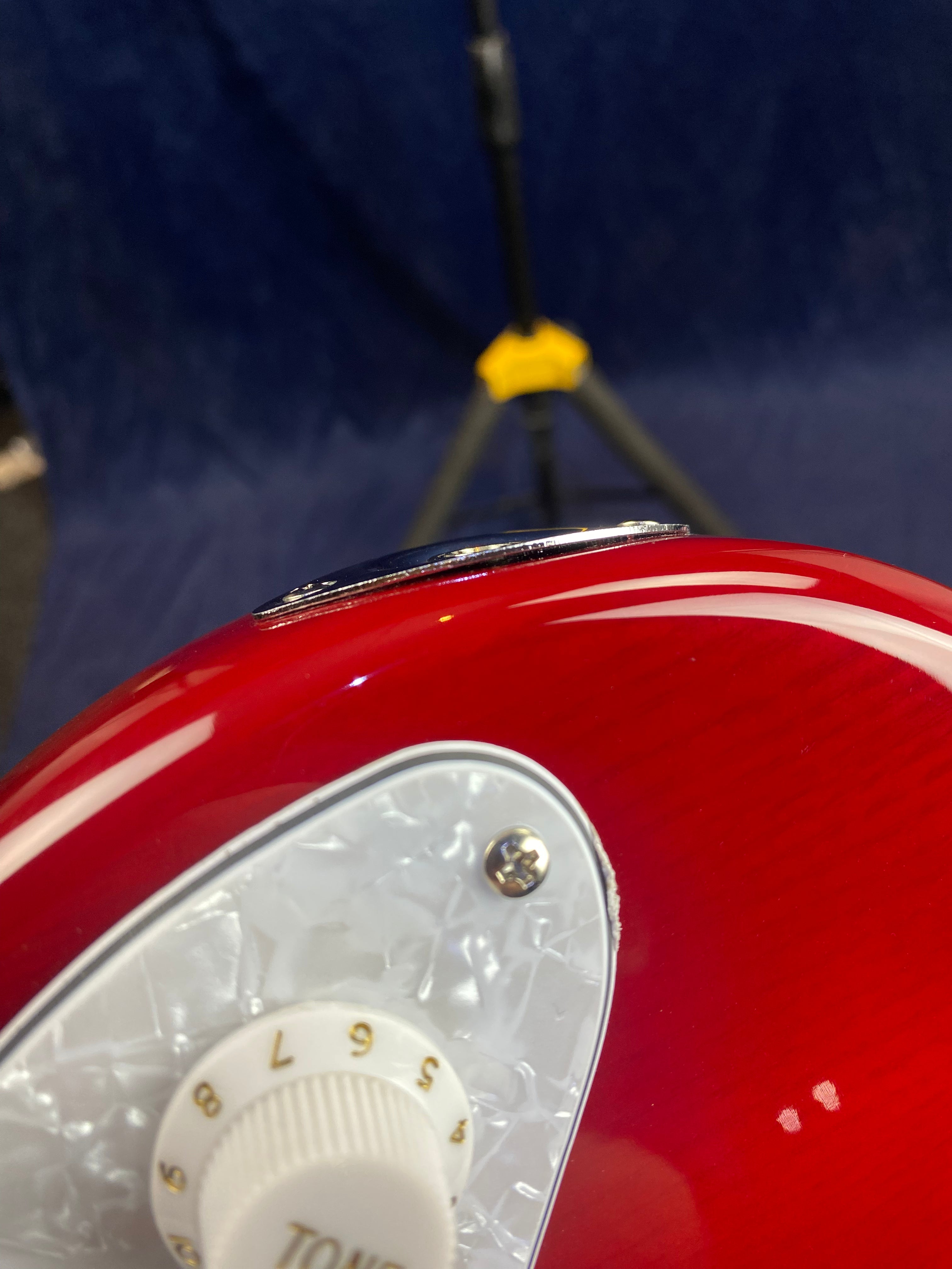 Close-up of a red electric guitar showing a white tone knob marked 1-10, part of a pearloid pickguard, and a metal strap button on the edge.