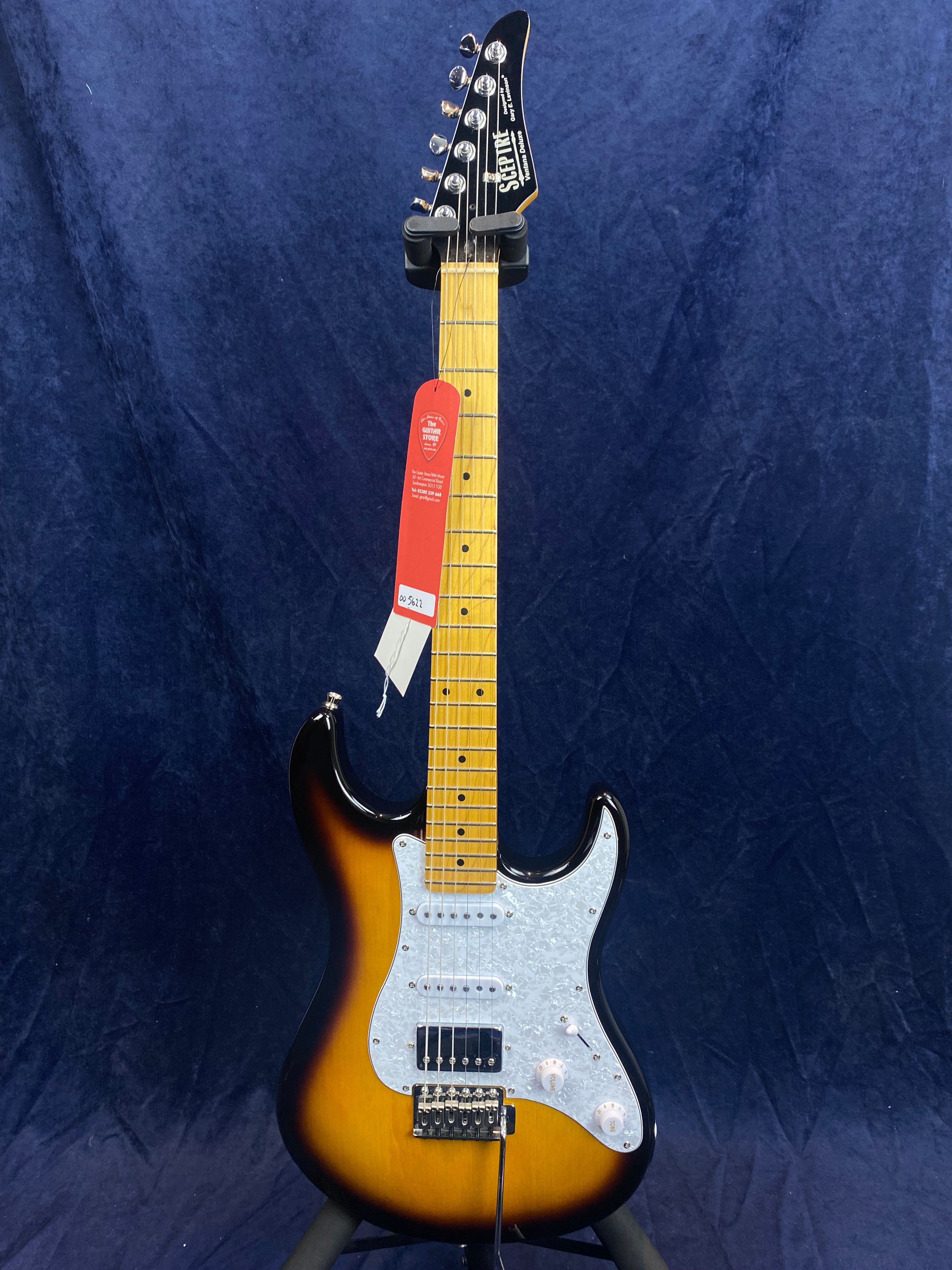 Sunburst electric guitar with a white pearloid pickguard, maple neck, six tuning pegs, three pickups, and a red tag hanging from the headstock.